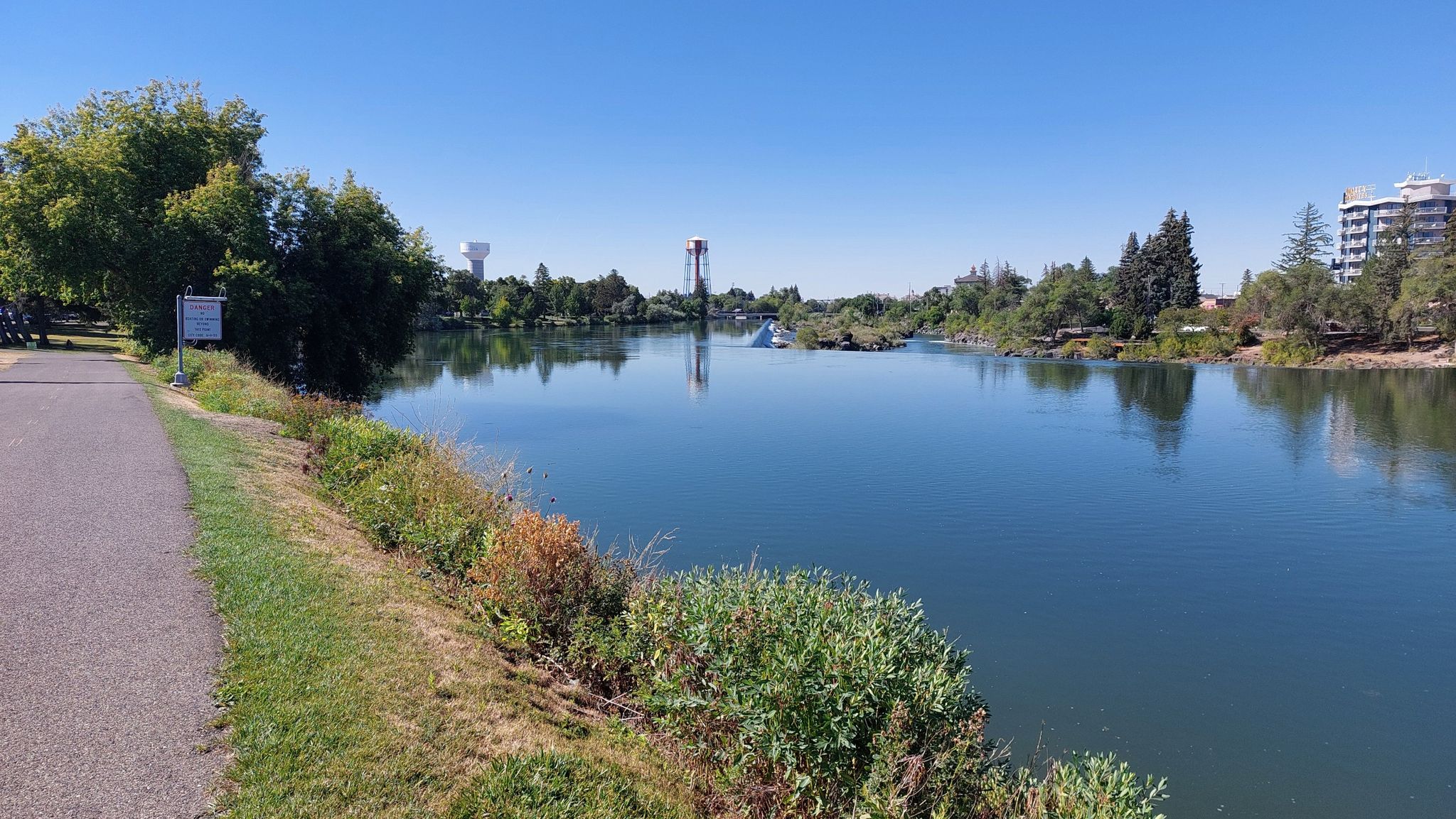 Calm river reflecting blue sky, with a paved path and green grassy banks. - Idaho Falls – Friendship Garden loop from Idaho Falls