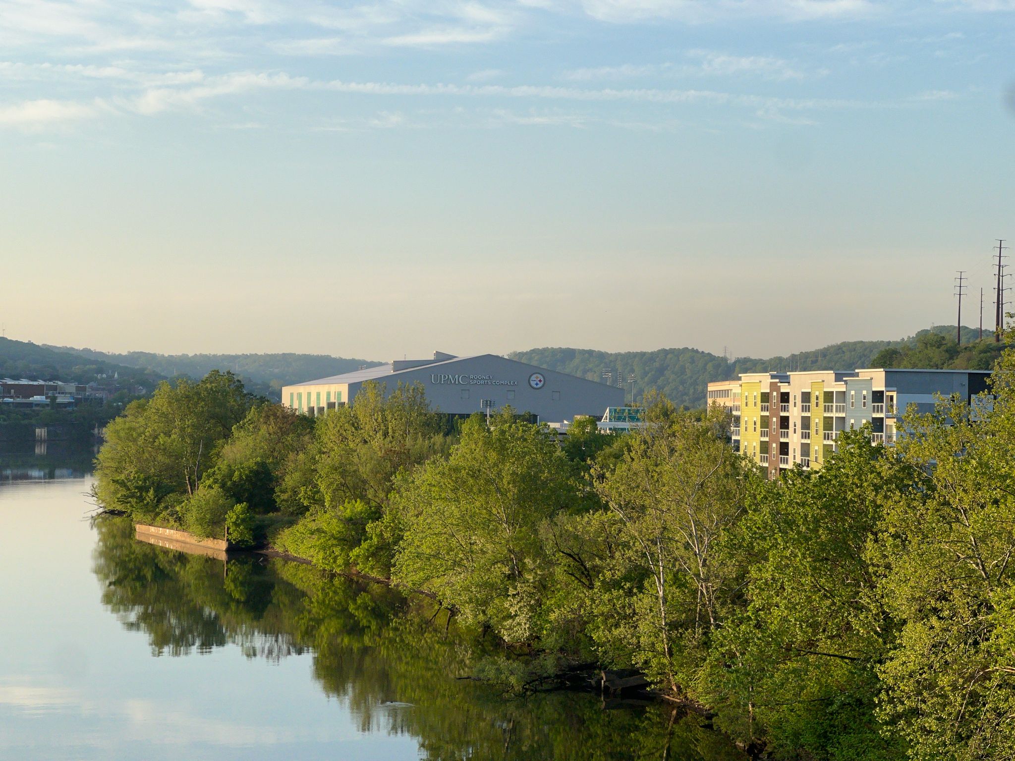 Calm river reflecting green trees and buildings on a sunny morning. - Great Allegheny Passage