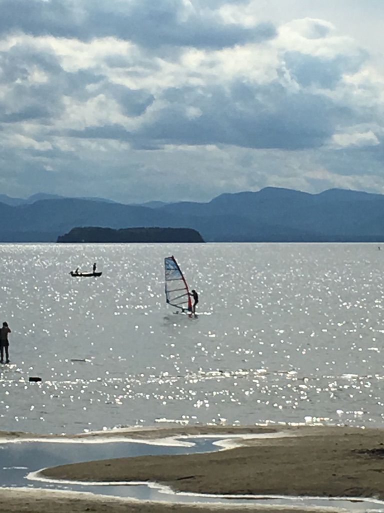 A windsurfer and people stand in sparkling water with distant mountains under clouds. - Barge Canal loop from Burlington