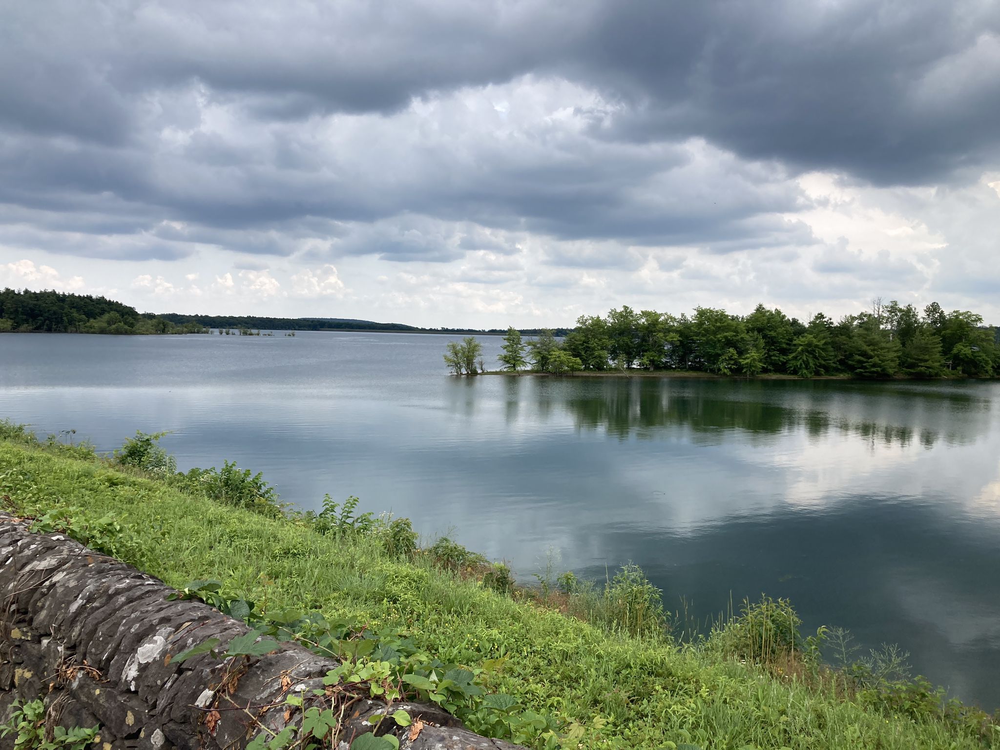 Overcast sky above a calm lake with forested shores and a stone wall. - Ashokan Rail Trail – Woodstock loop from Town of Woodstock