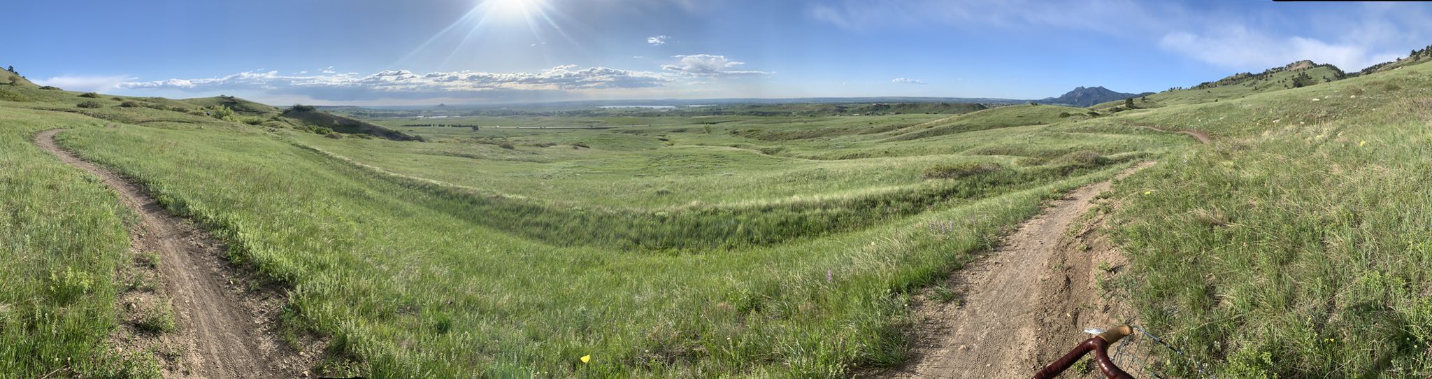 Panoramic view of sunlit green rolling hills with dirt trails under a blue sky. - Erie to Josephine Roche Open Space loop