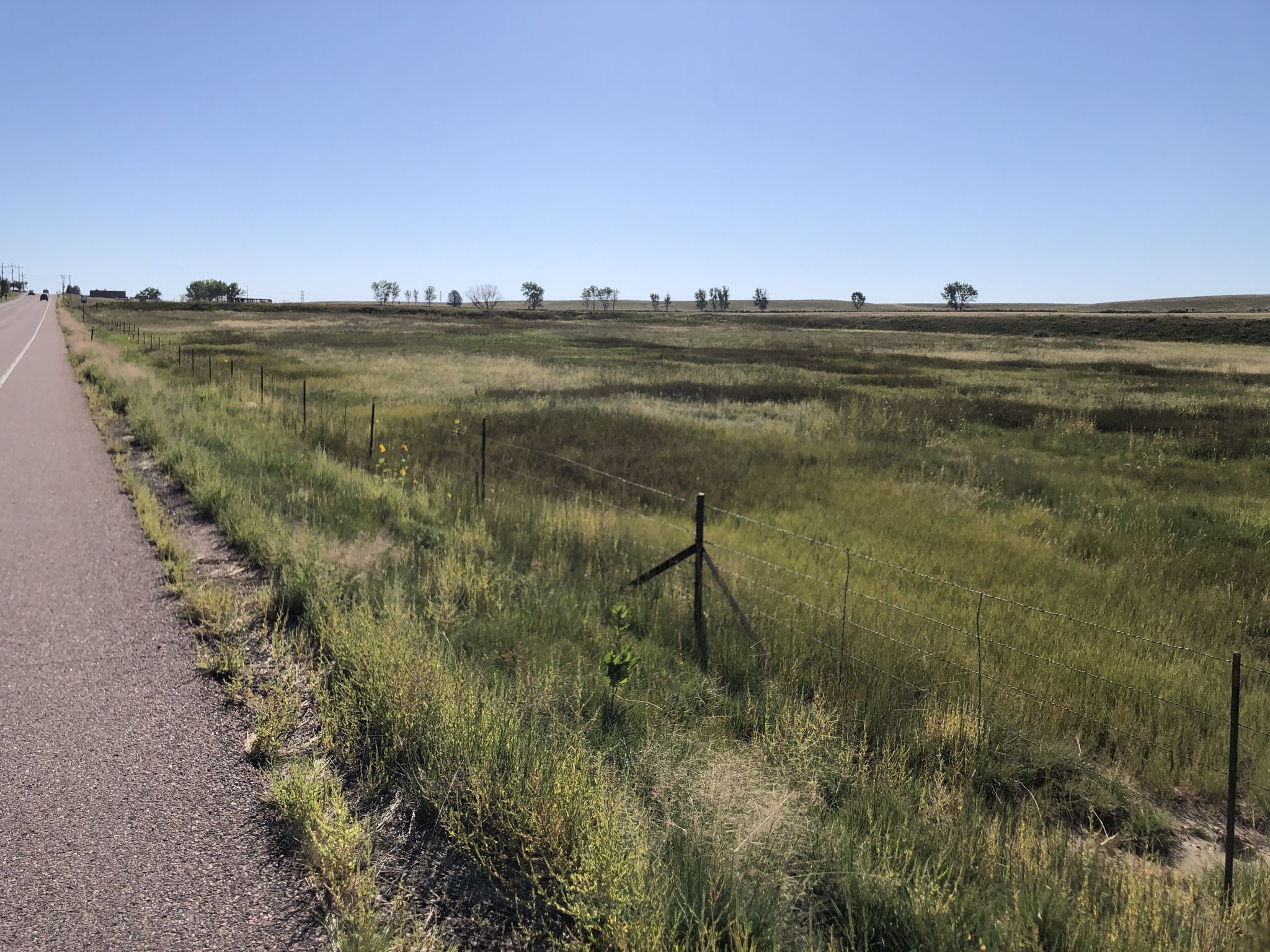 Paved road next to a vast green field with a fence under clear blue sky. - Broomfield County High Point – Eldorado Market loop from Flatiron Crossing