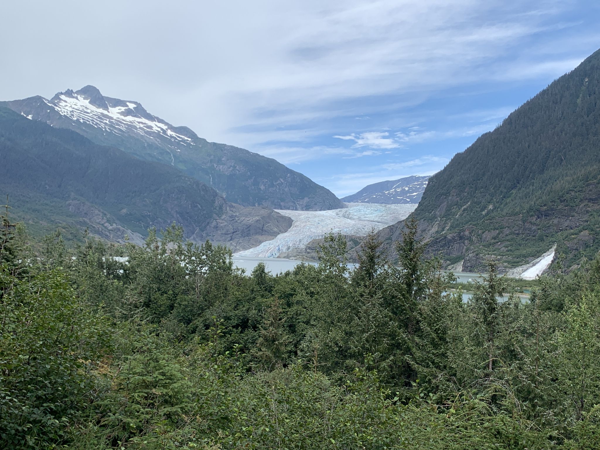 Wide view of a large glacier between mountains, with a lake and forest. - Trail of Time