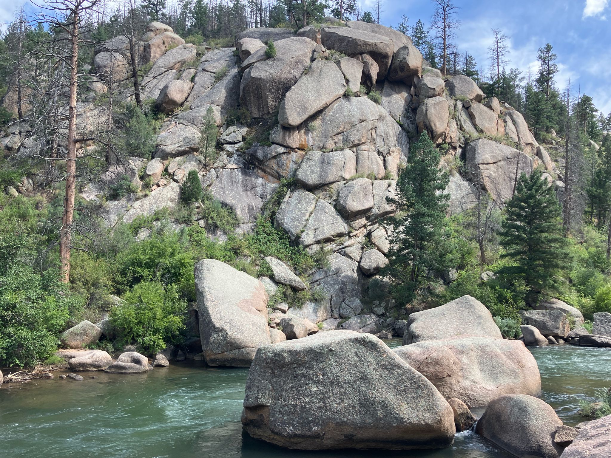 River flowing past large boulders and a rocky, forested hillside under bright sky. - South Buffalo Creek, Wellington Lake, & Stoney Pass Road gravel loop