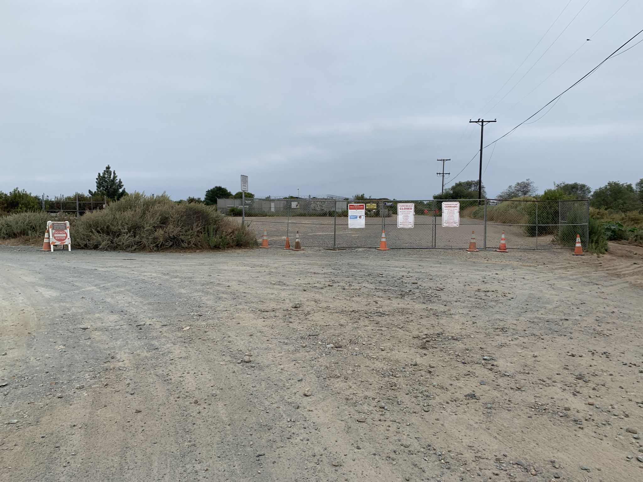 Dirt road blocked by a chain-link fence with signs under an overcast sky. - Spooners Mesa Trail Loop
