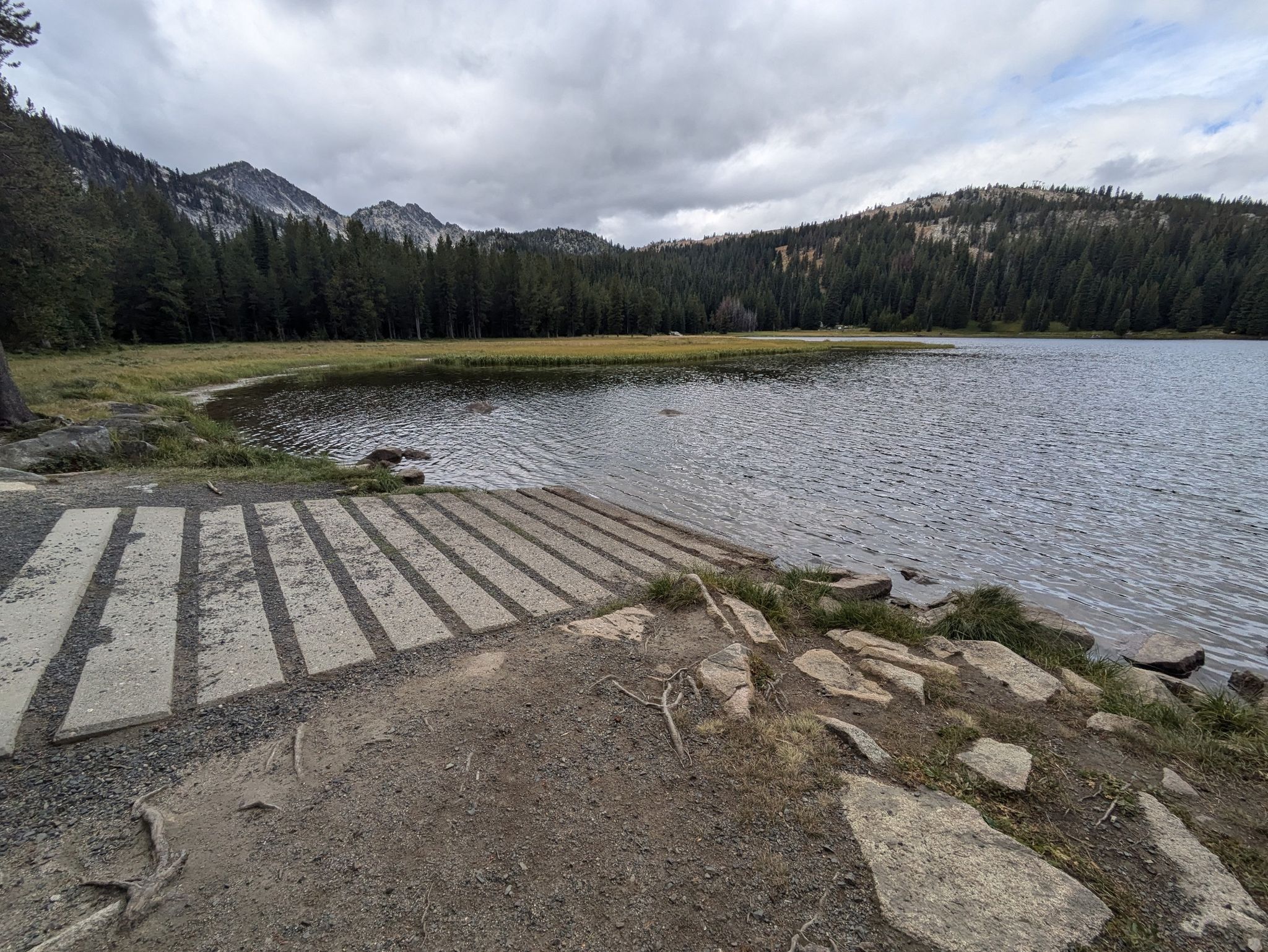 Concrete boat ramp leading into a lake, with forested mountains under a cloudy sky. - Elkhorn Crest, Crawfish Basin, and Hoffer Lakes Loop via Anthony Lake