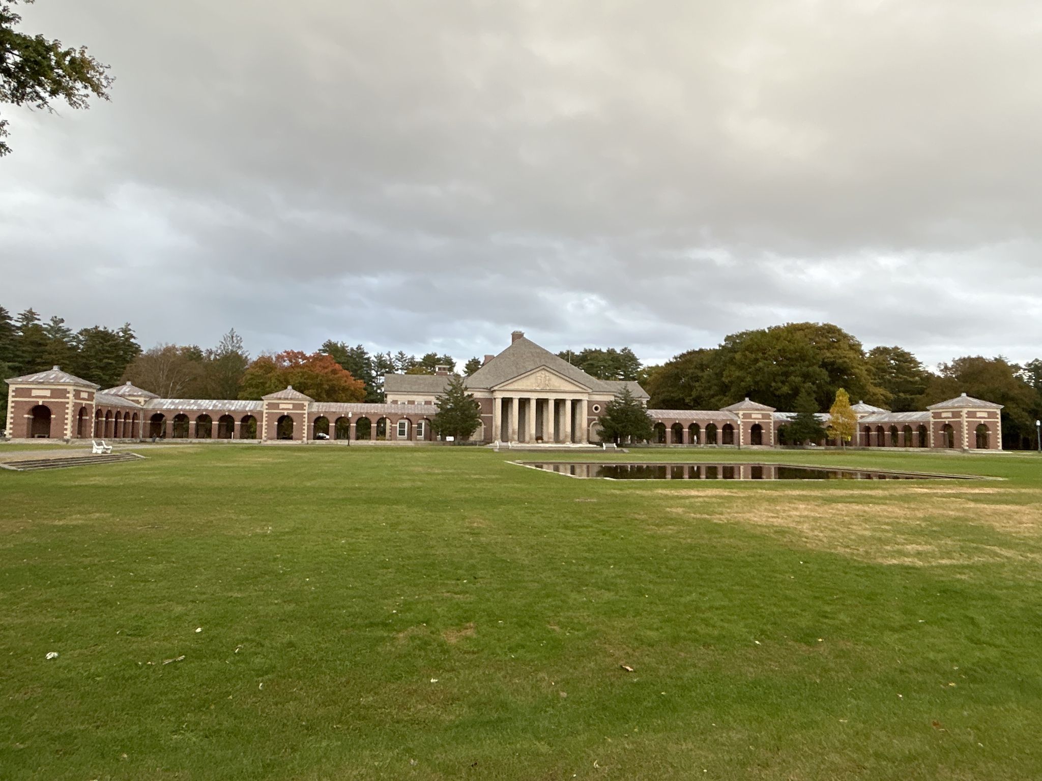 Large classical building with columns, long wings, green lawn, and pond under overcast sky. - Hall of Springs – Roosevelt Baths & Spa loop from Saratoga Performing Arts Center