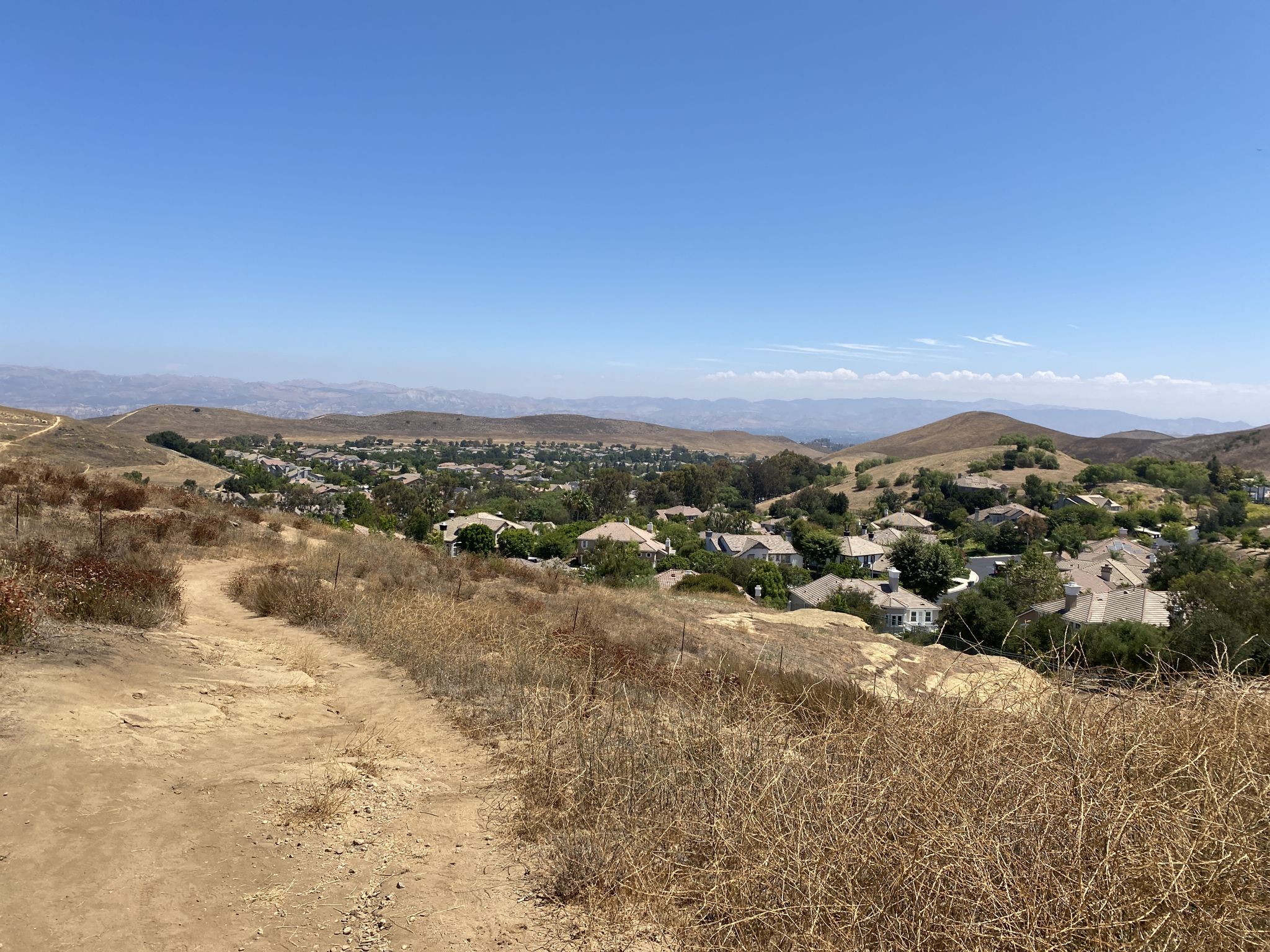 A dirt path on a dry hillside overlooking a residential valley under a clear sky. - Hiking loop from Bard Lake