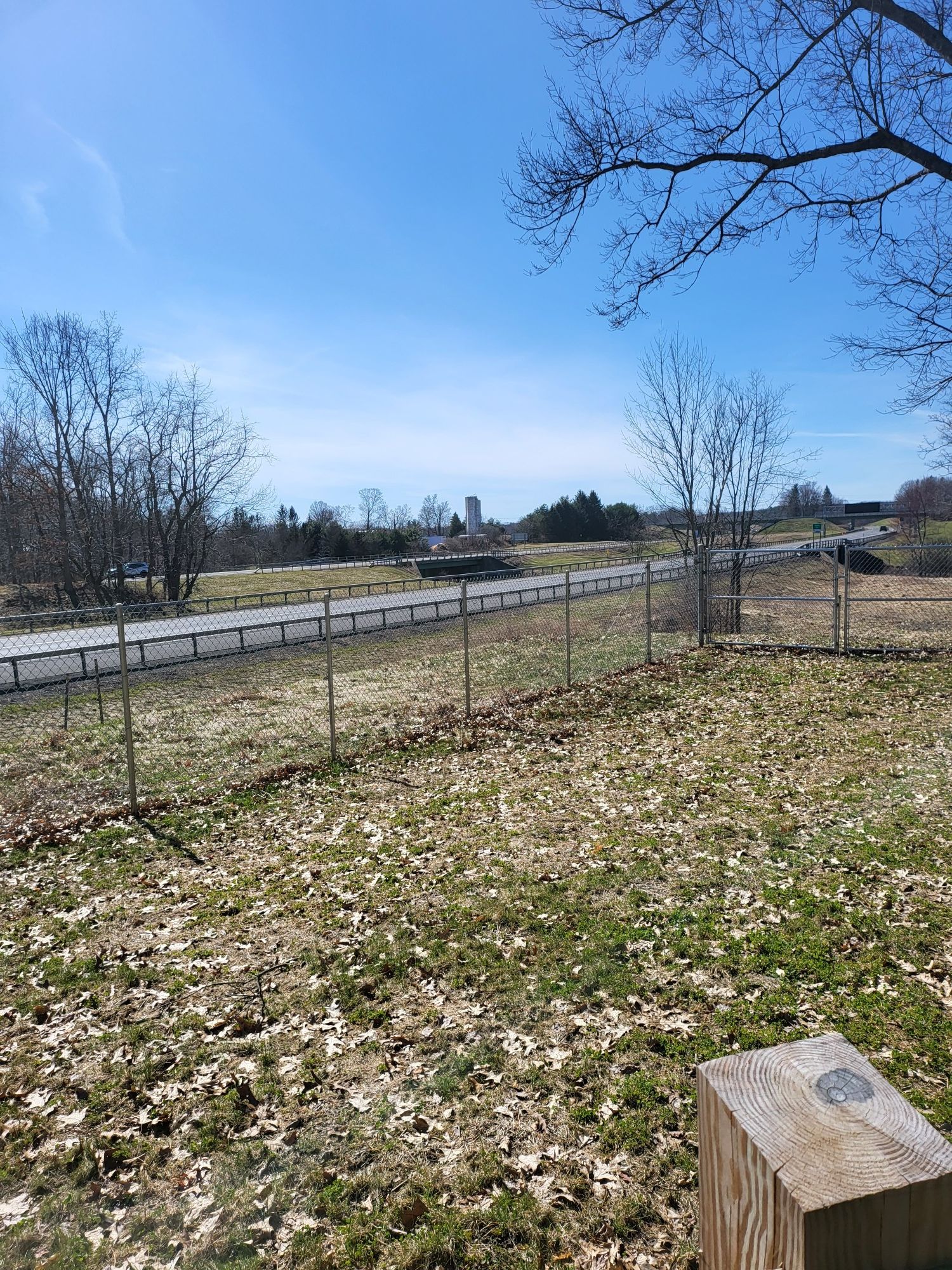 Grassy field with a fence, road, and distant buildings under a clear blue sky. - Views of Nassau Lake loop from North Chatham