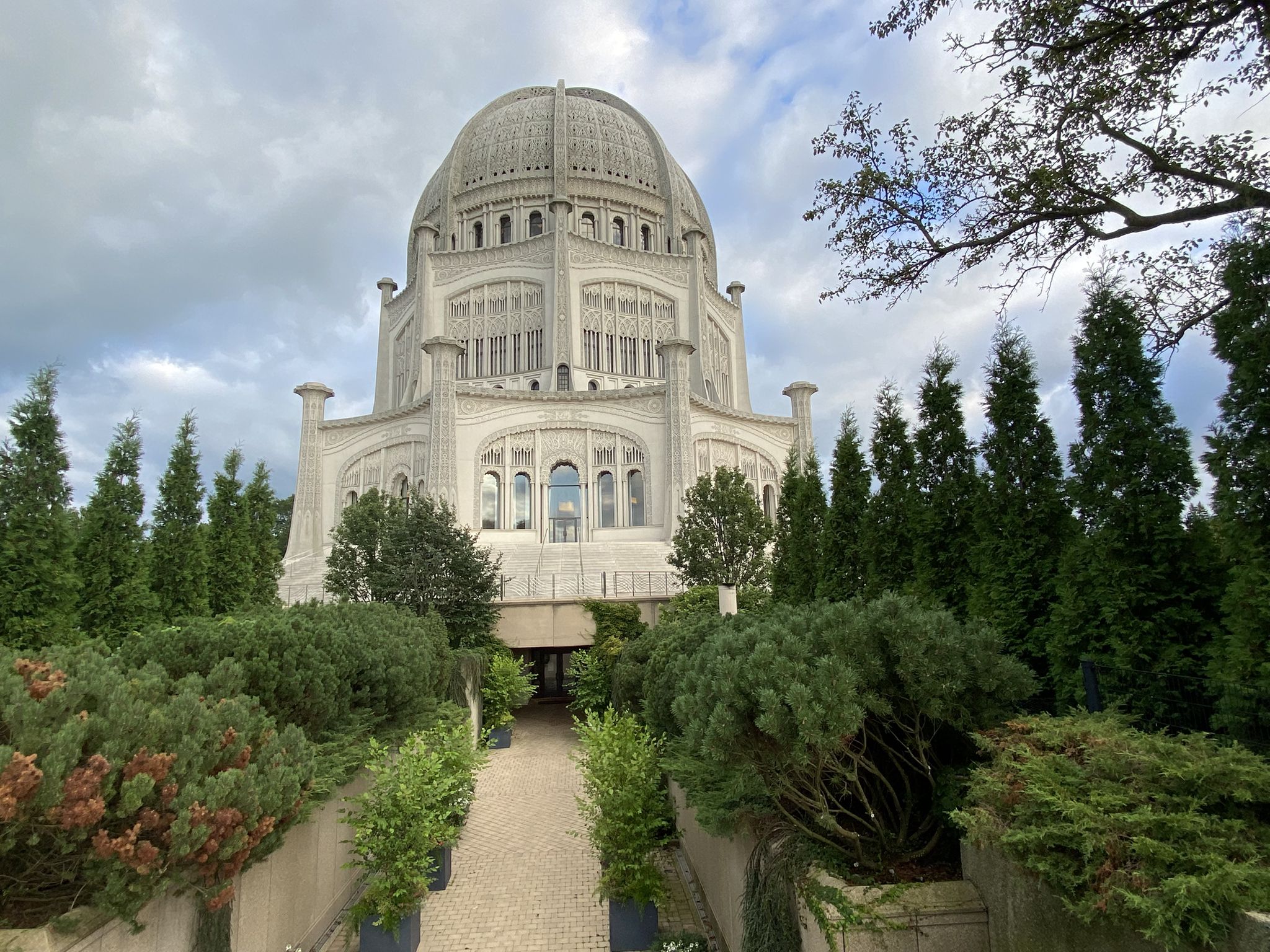 A grand white domed building surrounded by manicured green trees under a cloudy sky. - Baha'i Temple loop via North Shore Channel Trail
