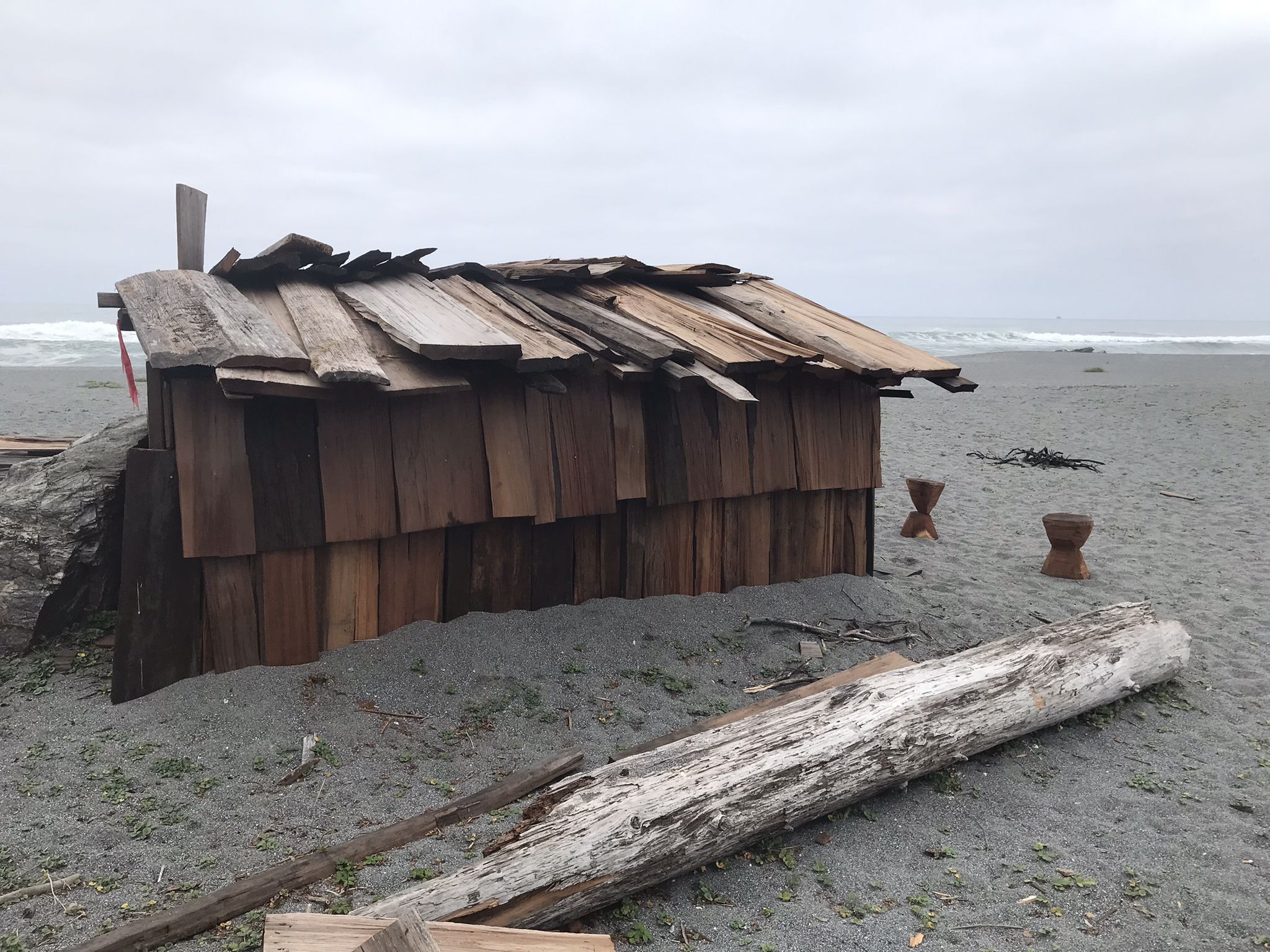 Rustic wooden shack on a sandy beach under an overcast sky with ocean waves. - California Coastal Trail: Stone Lagoon