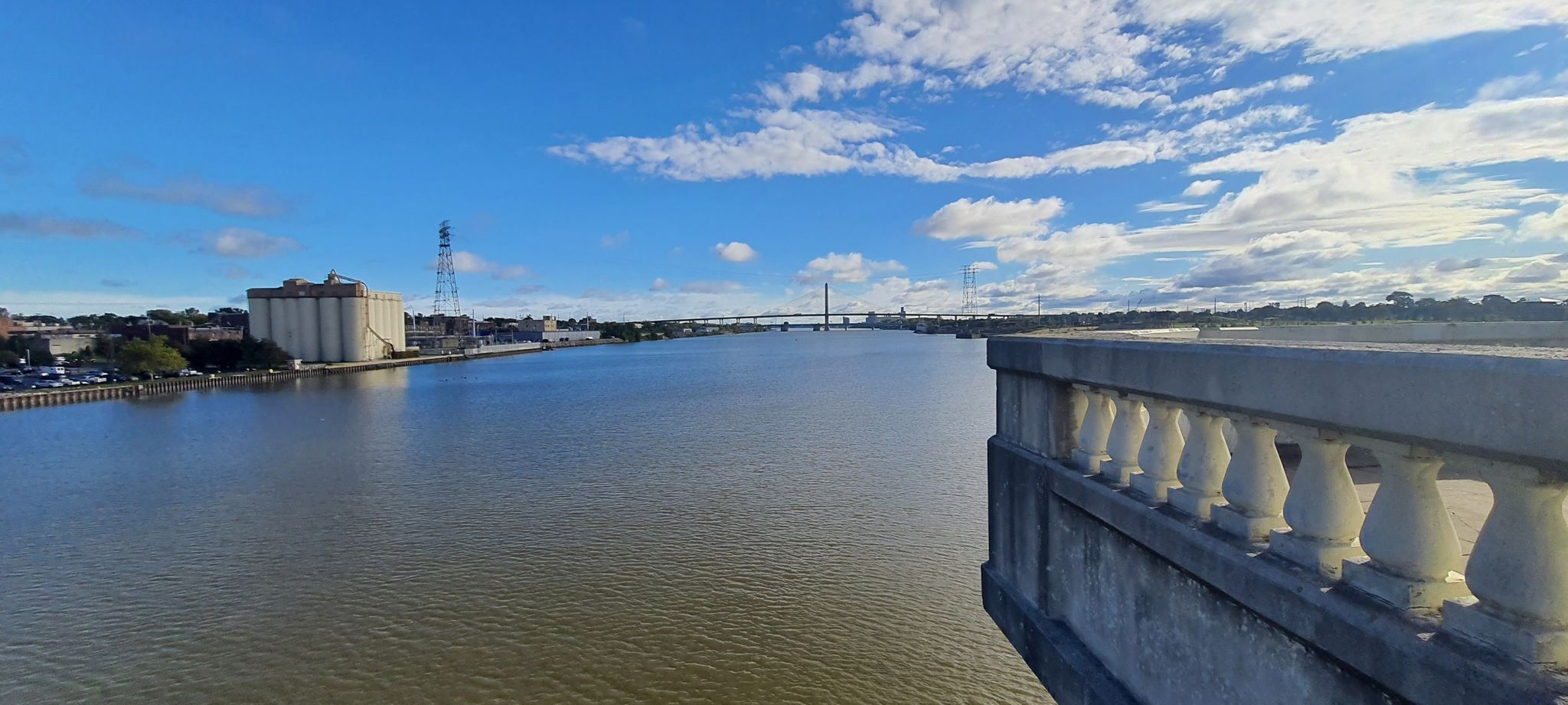 Wide river with distant bridge and industrial buildings under blue sky. - Glass City Metropark loop