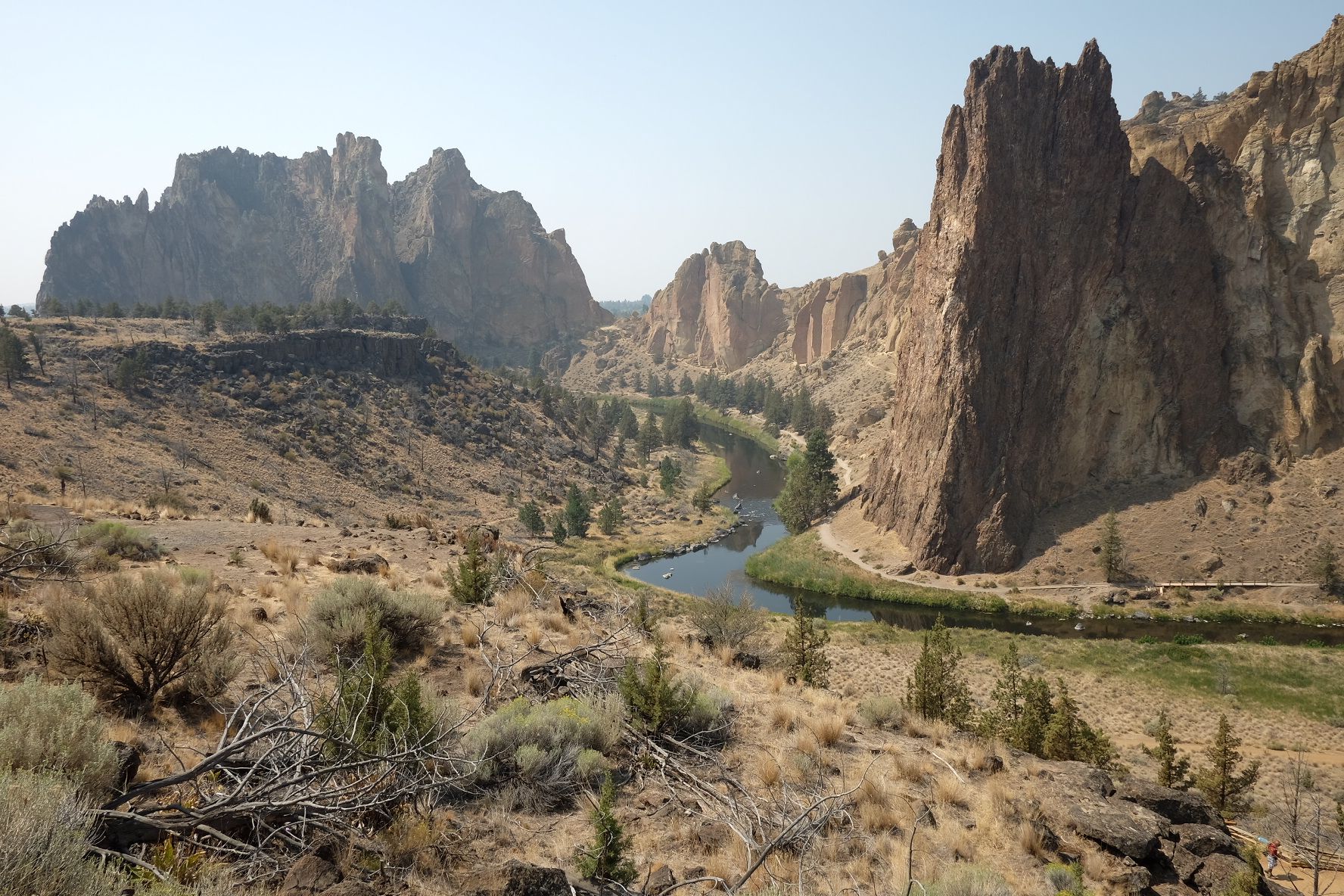 River flows through a dry canyon with towering rock formations under a hazy sky. - Smith Rock State Park – View of Smith Rock State Park loop from Smith Rock State Park