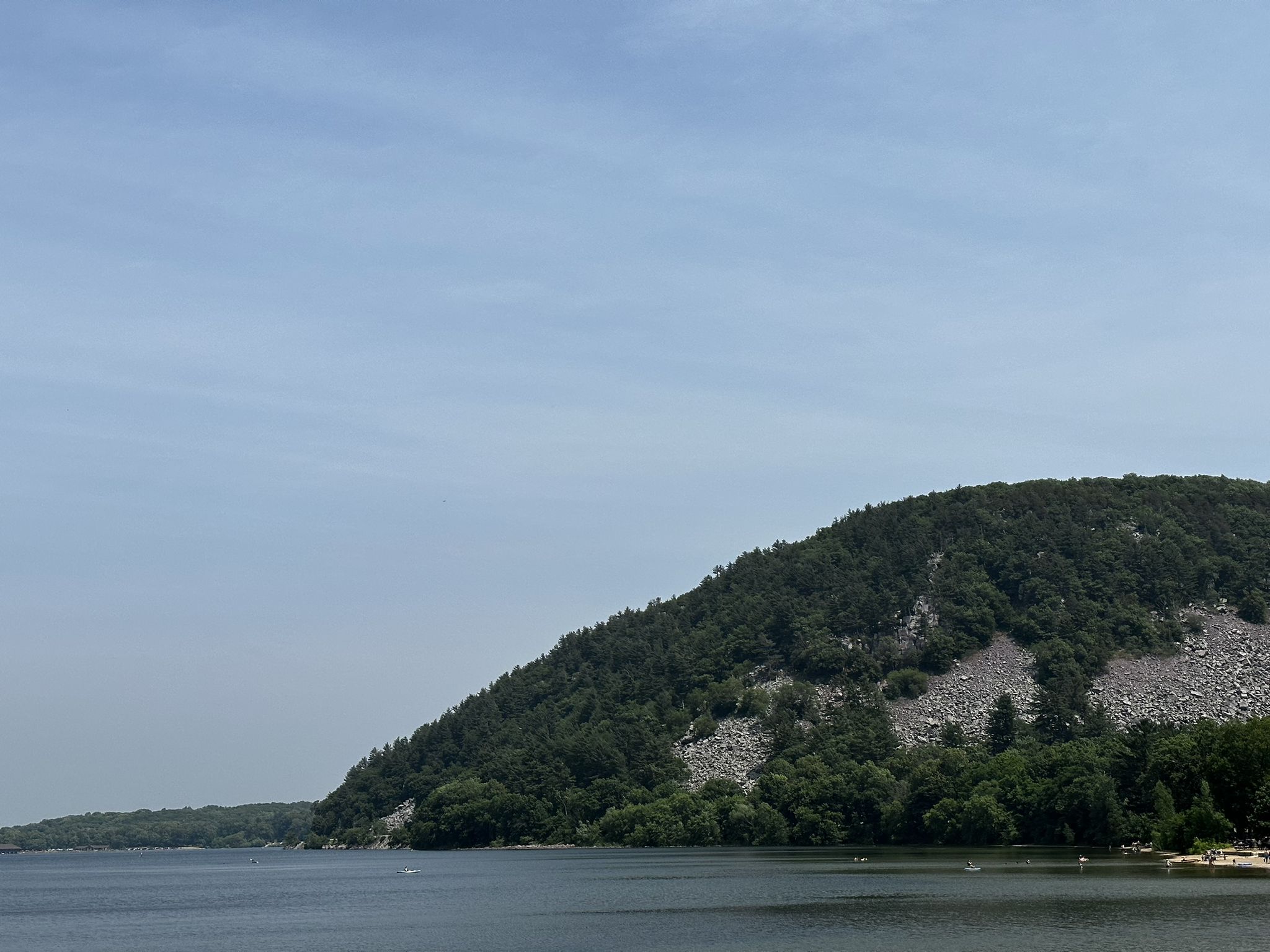 A large lake with a forested hill and rock slides under a clear sky. - Ice Age Trail: Devil's Lake East Bluff Loop
