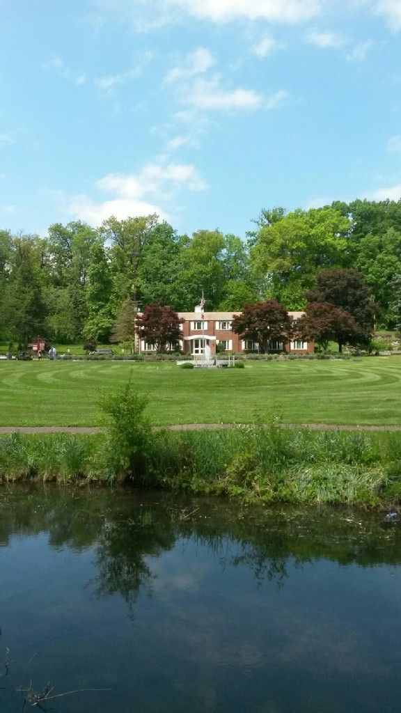 Sunny view of a large house and patterned lawn reflected in calm water. - Running loop from Canton