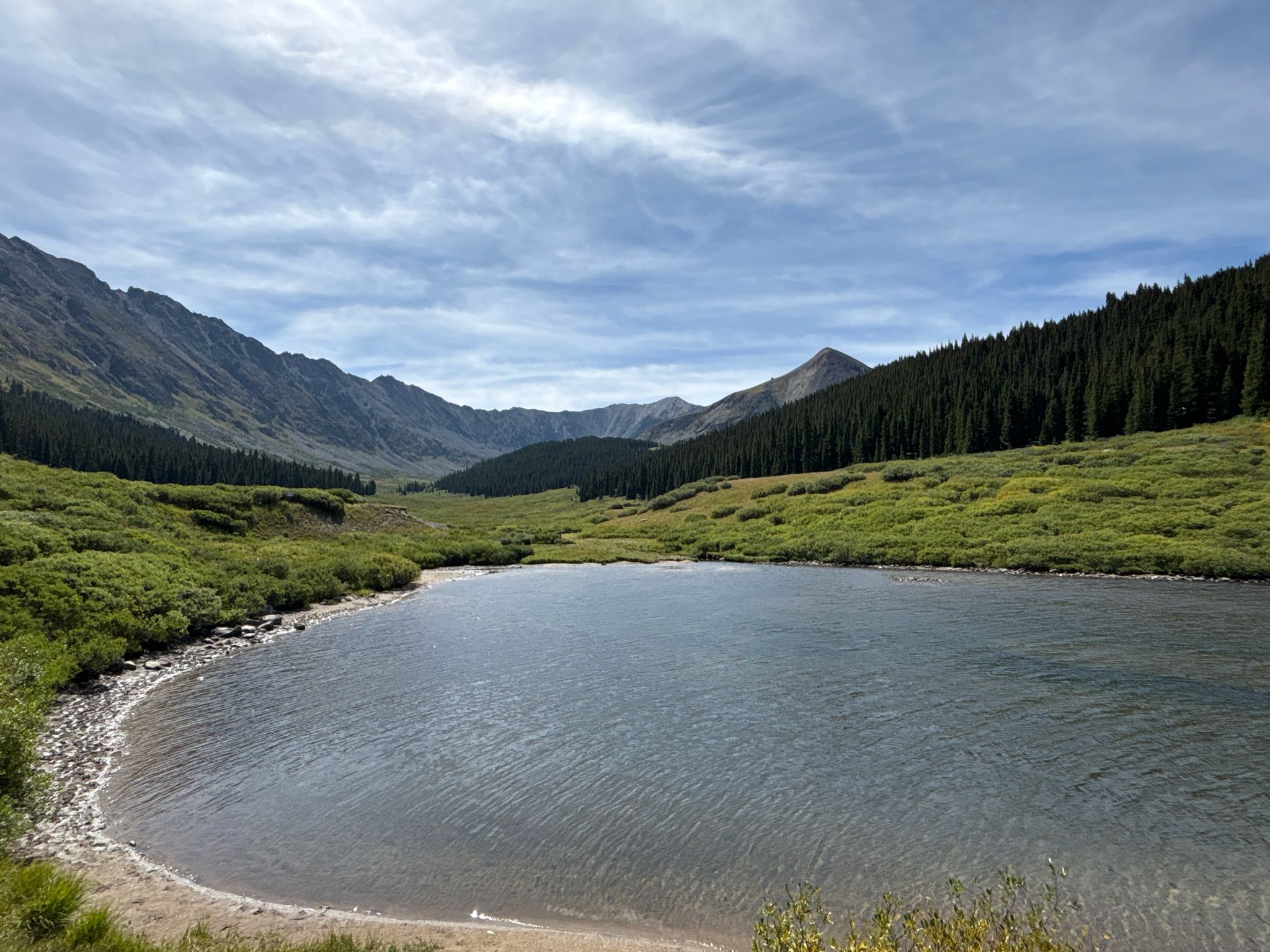 Calm lake in a mountain valley surrounded by green slopes and pine trees. - Clinton Gulch Reservoir Trail