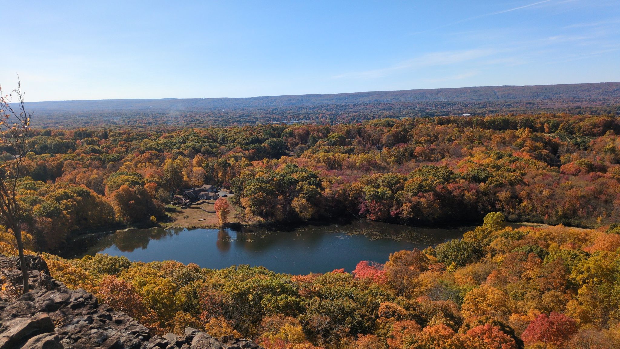 Sunny panoramic view of a small lake surrounded by vibrant autumn forest. - Metacomet Trail