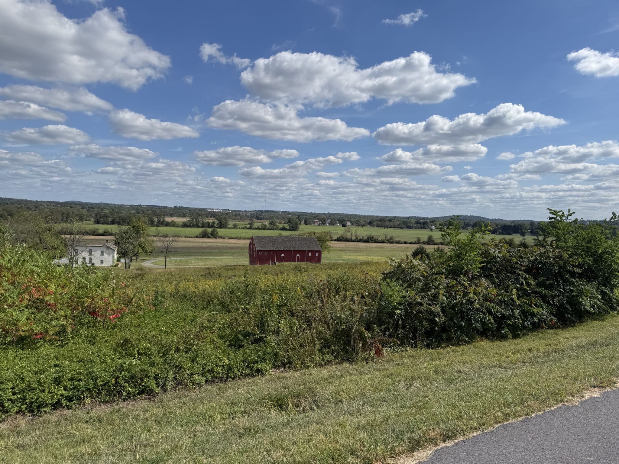 Red barn and white house in green fields under a bright, cloudy sky. - Eternal Light Peace Memorial – Jennie Wade House loop from Gettysburg & Harrisburg Railroad Depot