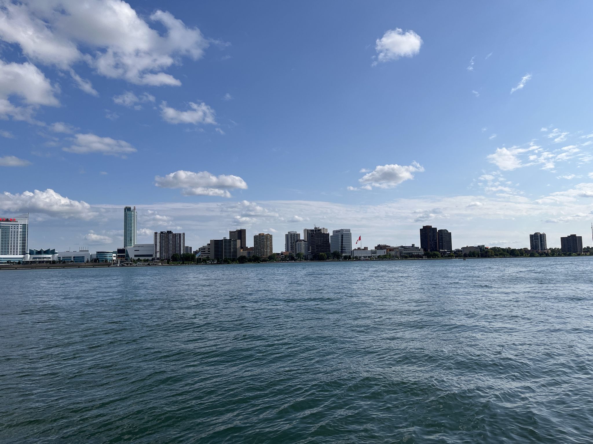 City skyline across a wide river under a bright blue sky with clouds. - Iron Belle Trail: Belle Isle Loop