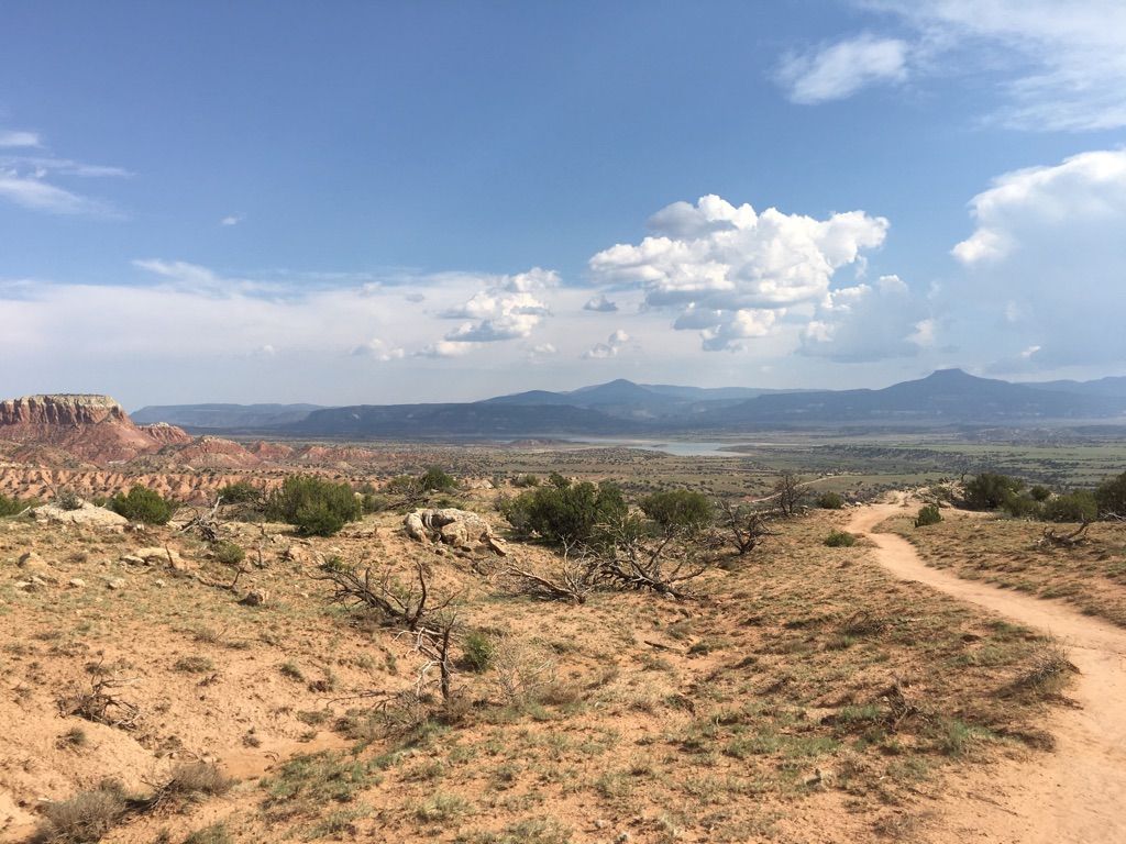 A dirt path winds through a vast desert landscape under a cloudy sky. - Chimney Rock Trail