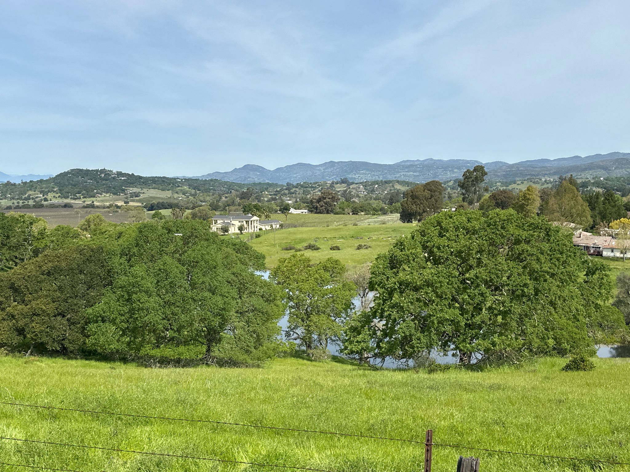 A serene landscape with green fields, trees, a lake, and distant houses under a bright sky. - Skyline and Manzanita Trail Loop