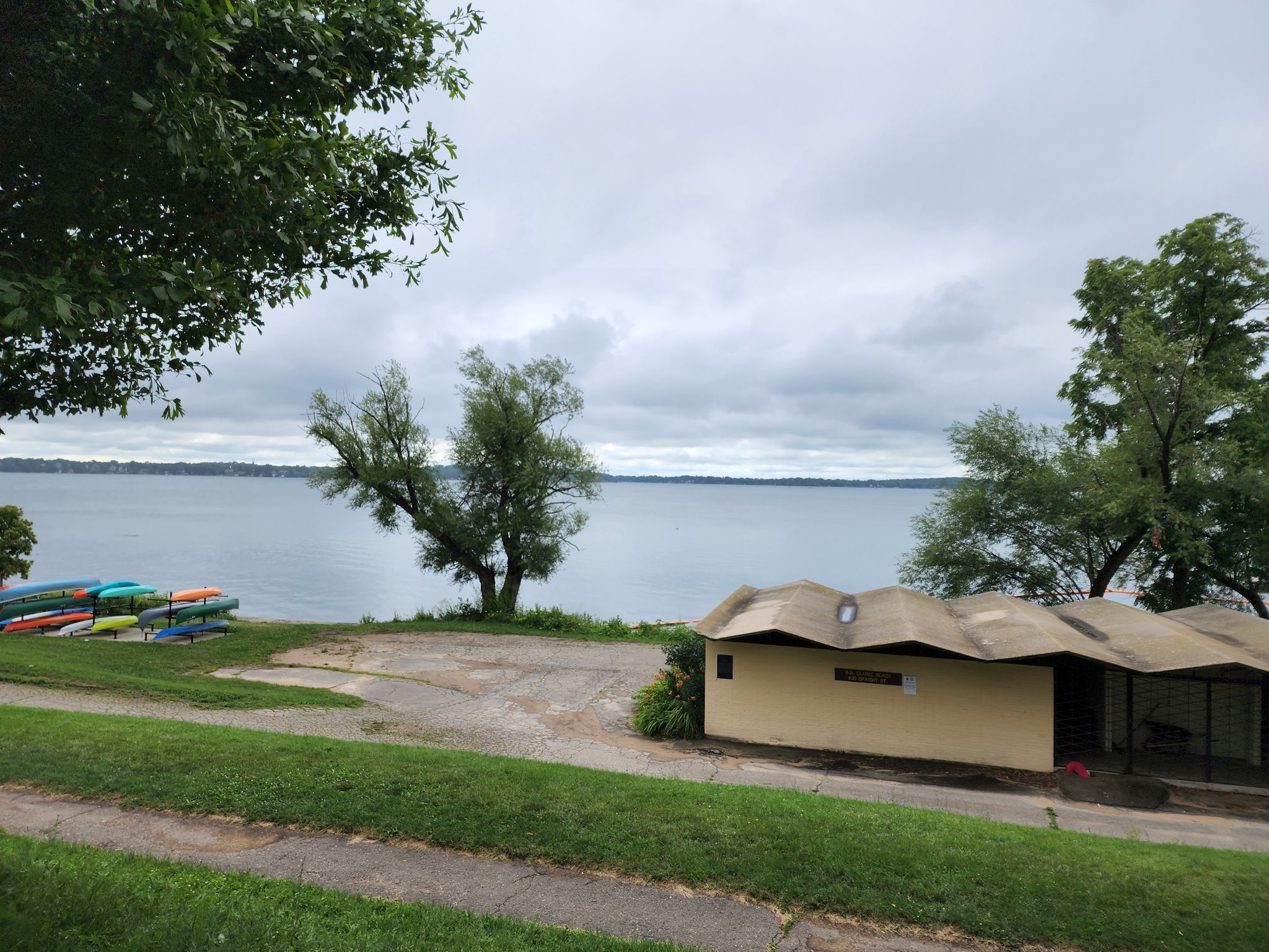 Overcast view of a lake, building, colorful kayaks, and green lawn. - Yahara River loop from Breese Stevens Field