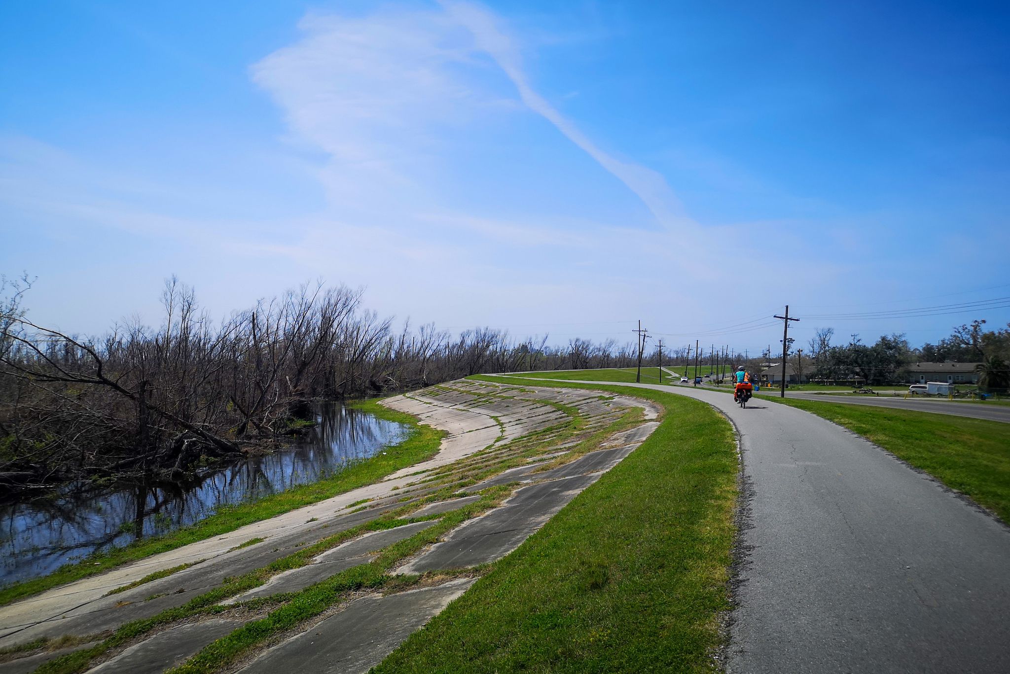 A paved path curves beside a waterway with bare trees and a cyclist. - Roadbike loop from Kenner