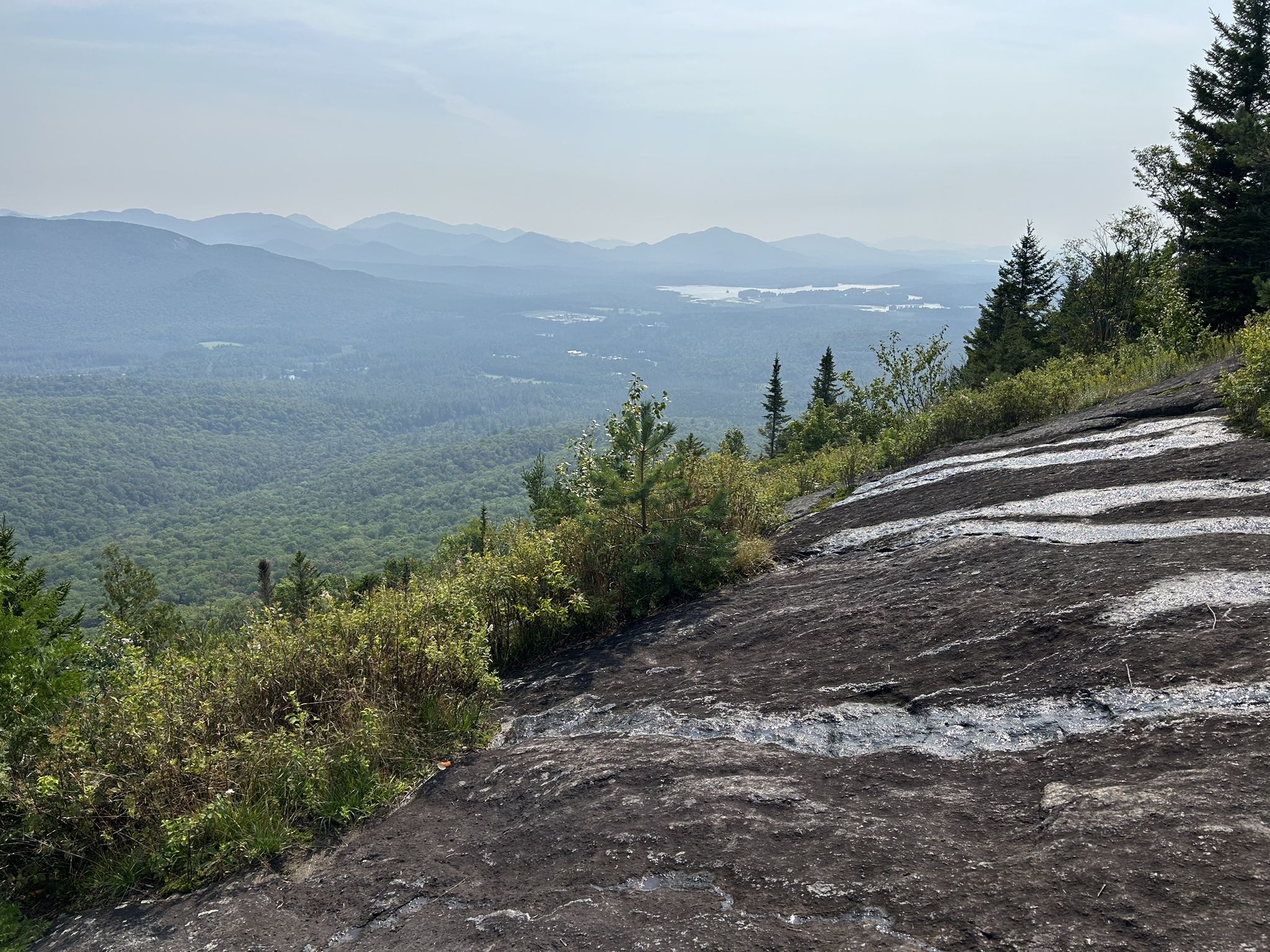 Rocky mountain slope overlooking a hazy forested valley and distant lake. - Haystack Mountain via Jackrabbit Trail
