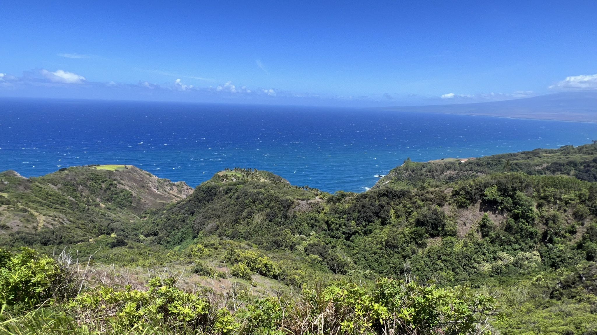 Expansive view of lush green hills meeting a vibrant blue ocean under clear sky. - Kahekili Highway – Kahekili Highway loop from Wailuku
