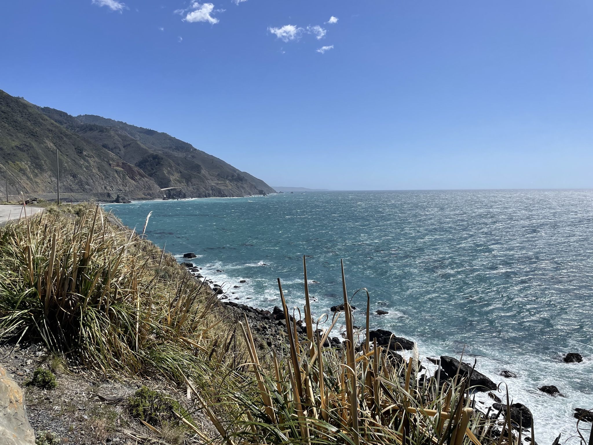 Rough ocean waves crash against a rocky coast with a road and mountains. - Los Burros and South Coast Ridge Road Loop