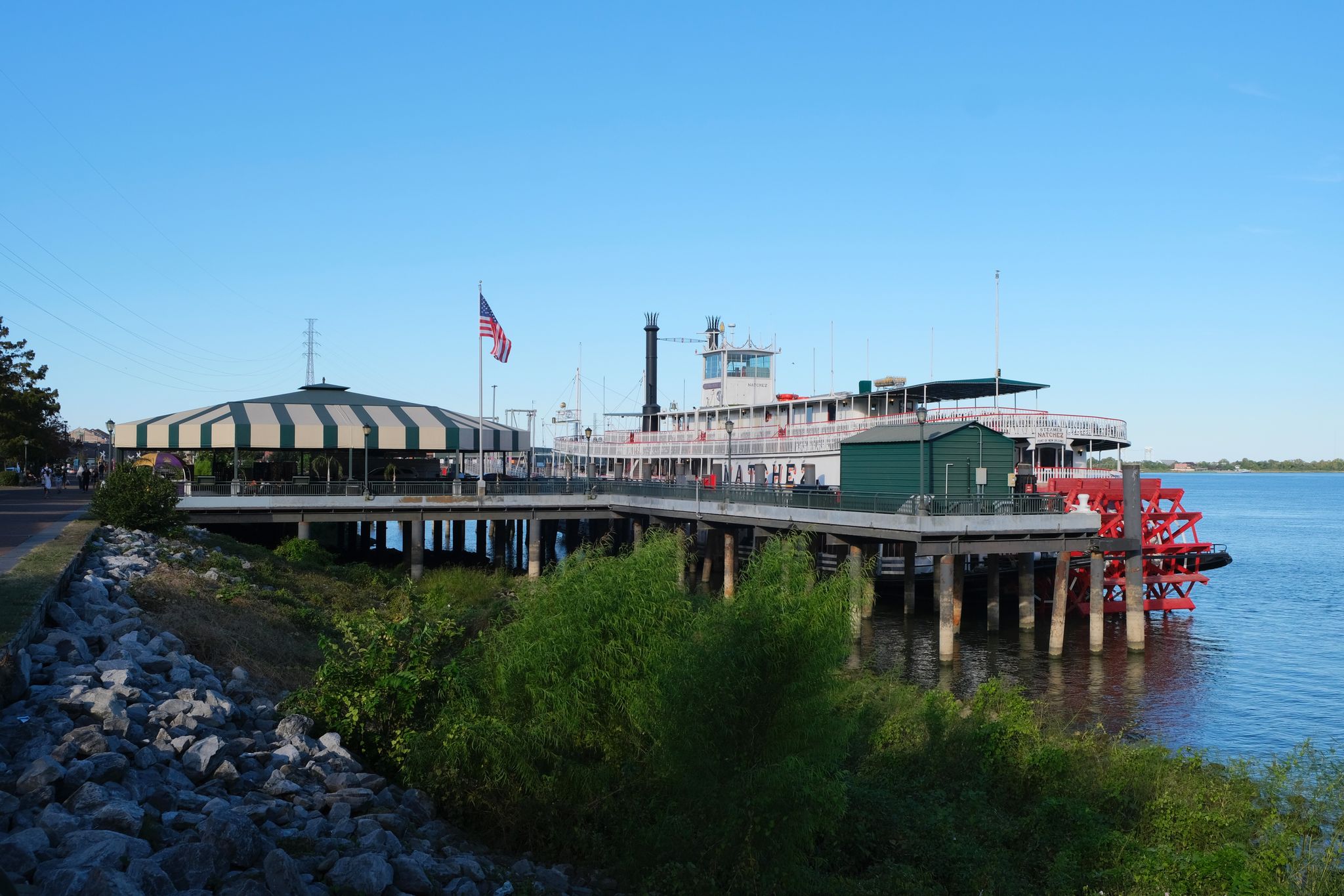 A large paddlewheel boat docked by a pier on a sunny day. - Steamboat Natchez – Royal Street, New Orleans loop from New Orleans