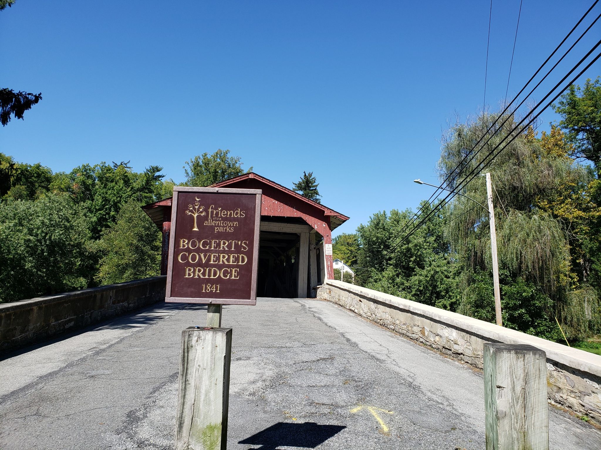 A sign stands before a red covered bridge entrance under a clear blue sky. - Bogert Covered Bridge – Nice bridge with trail by river loop from Lehigh Valley Hospital