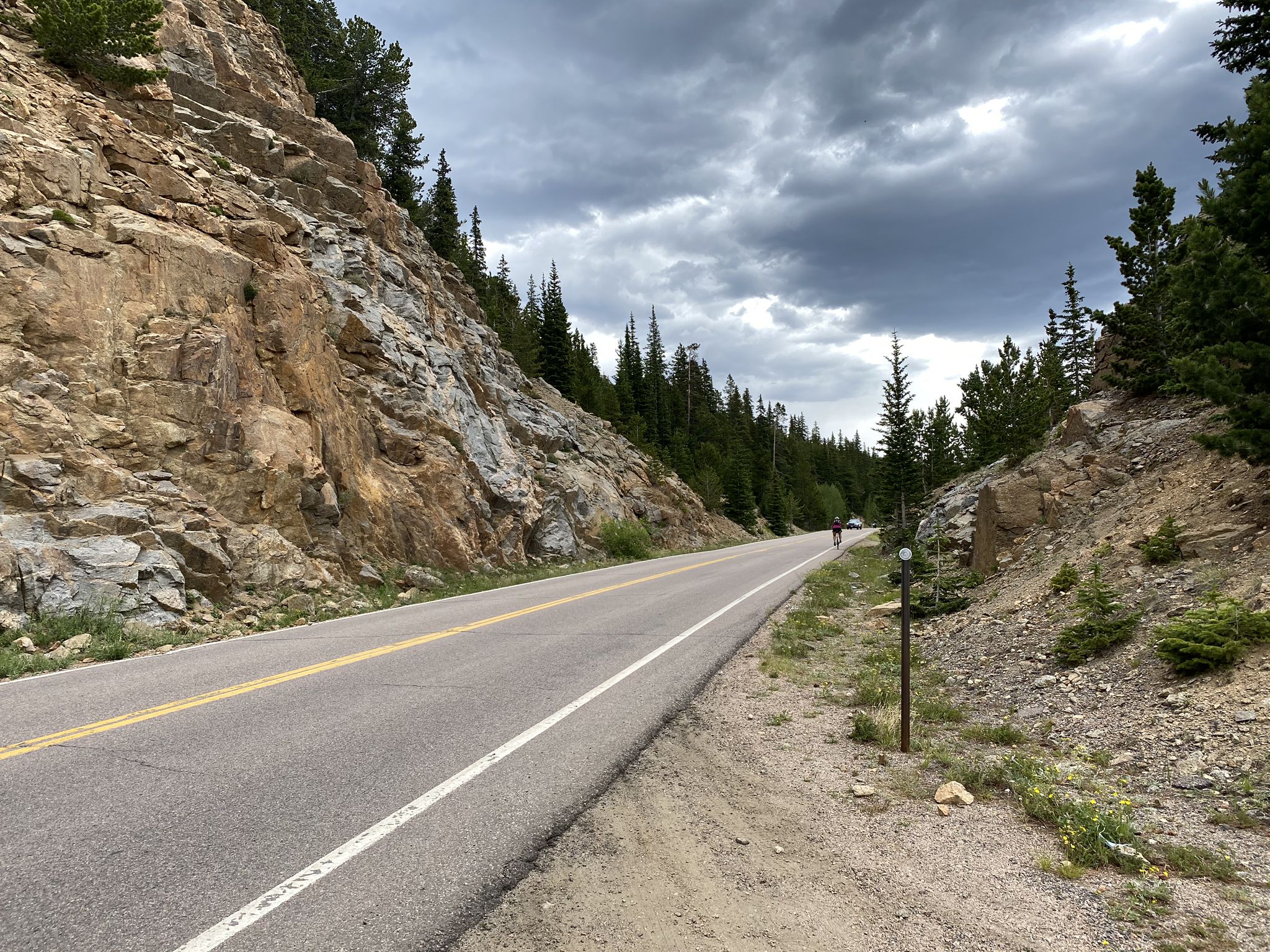 A winding mountain road with a distant cyclist under a cloudy sky. - Idaho Springs to Juniper Pass via Echo Lake