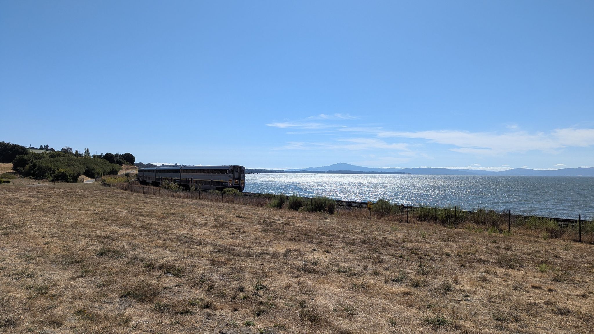 Train cars parked beside a sparkling bay with distant mountains under bright sun. - San Francisco Bay Trail