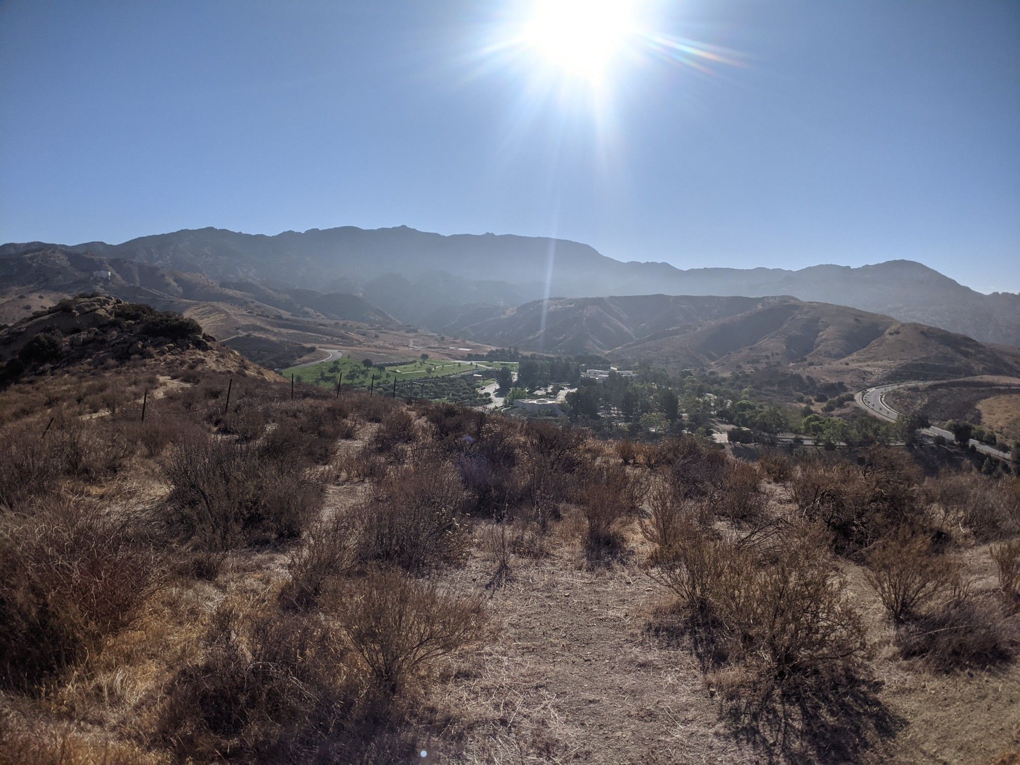 Bright sun over a valley with green fields and distant mountains. - Chumash Park loop from Santa Susana