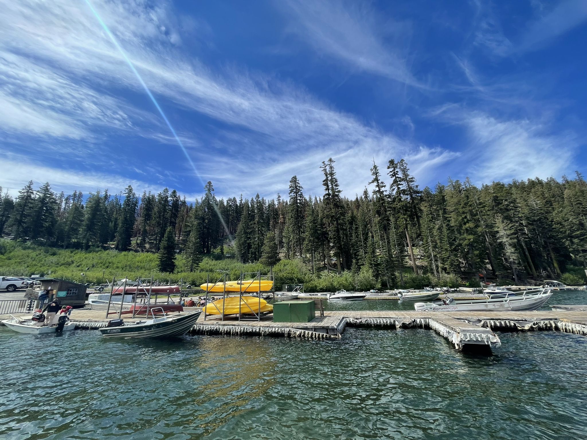 Boats and kayaks docked on a lake, surrounded by dense forest on a sunny day. - Pacific Crest Trail: Echo Lake to Lake of the Woods