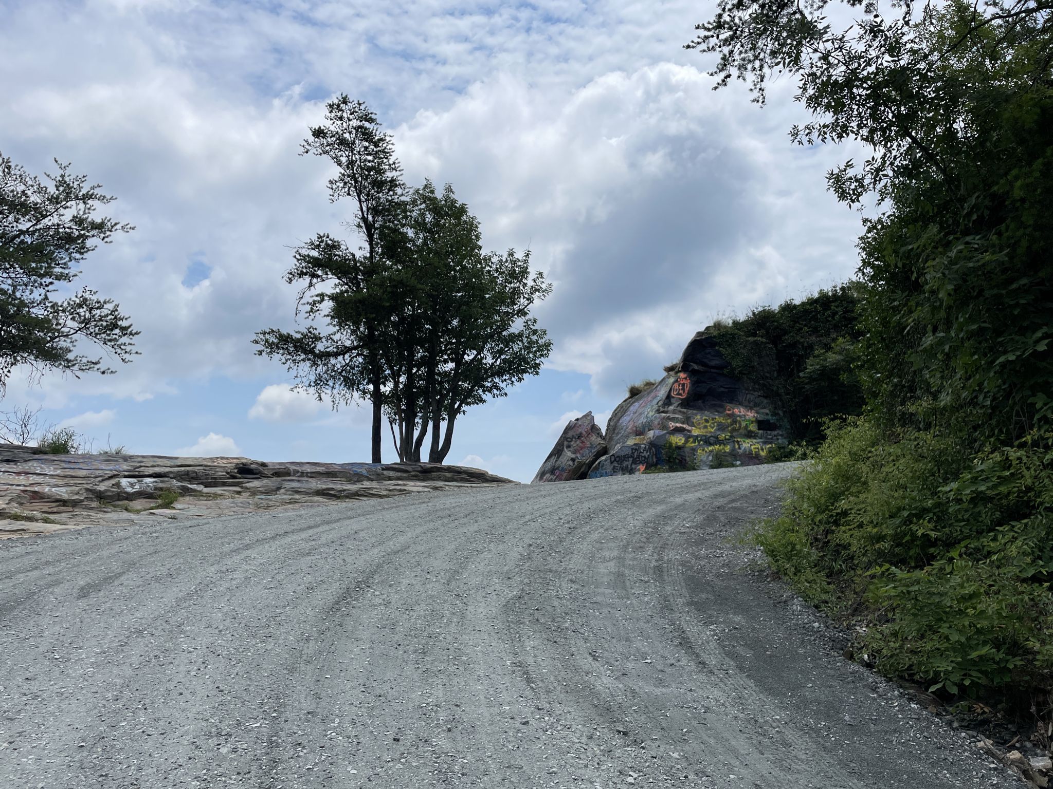 Gravel road winding uphill past rocks and trees under a cloudy sky. - Currahee Mountain