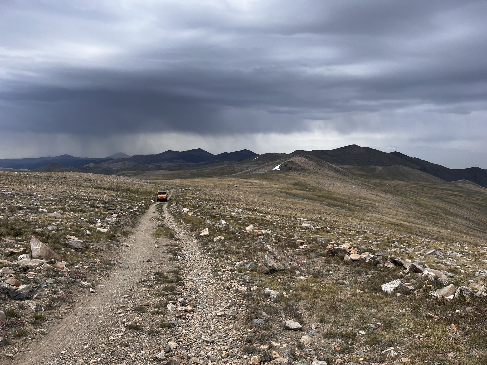Orange vehicle on a dirt road, stormy sky over distant mountains. - White Mountain Peak Trail