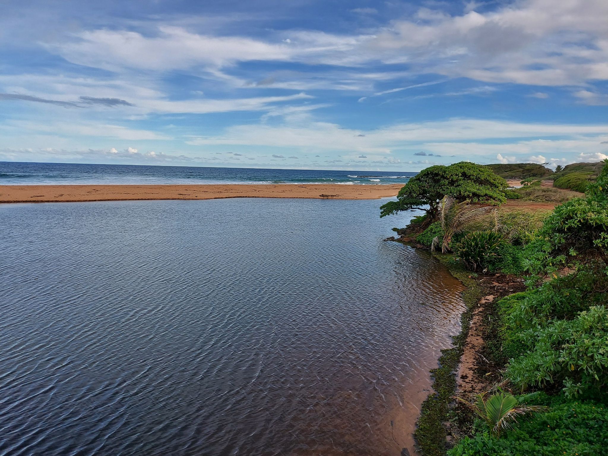 Calm river meeting a sandy beach and ocean under a partly cloudy sky. - Ke Ala Hele Makalae