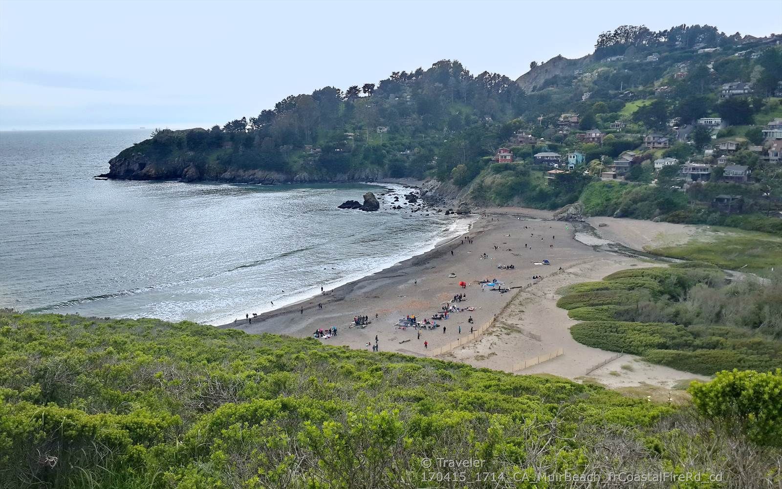 Sunny beach with many people, ocean waves, and distant houses. - Pirate's Cove