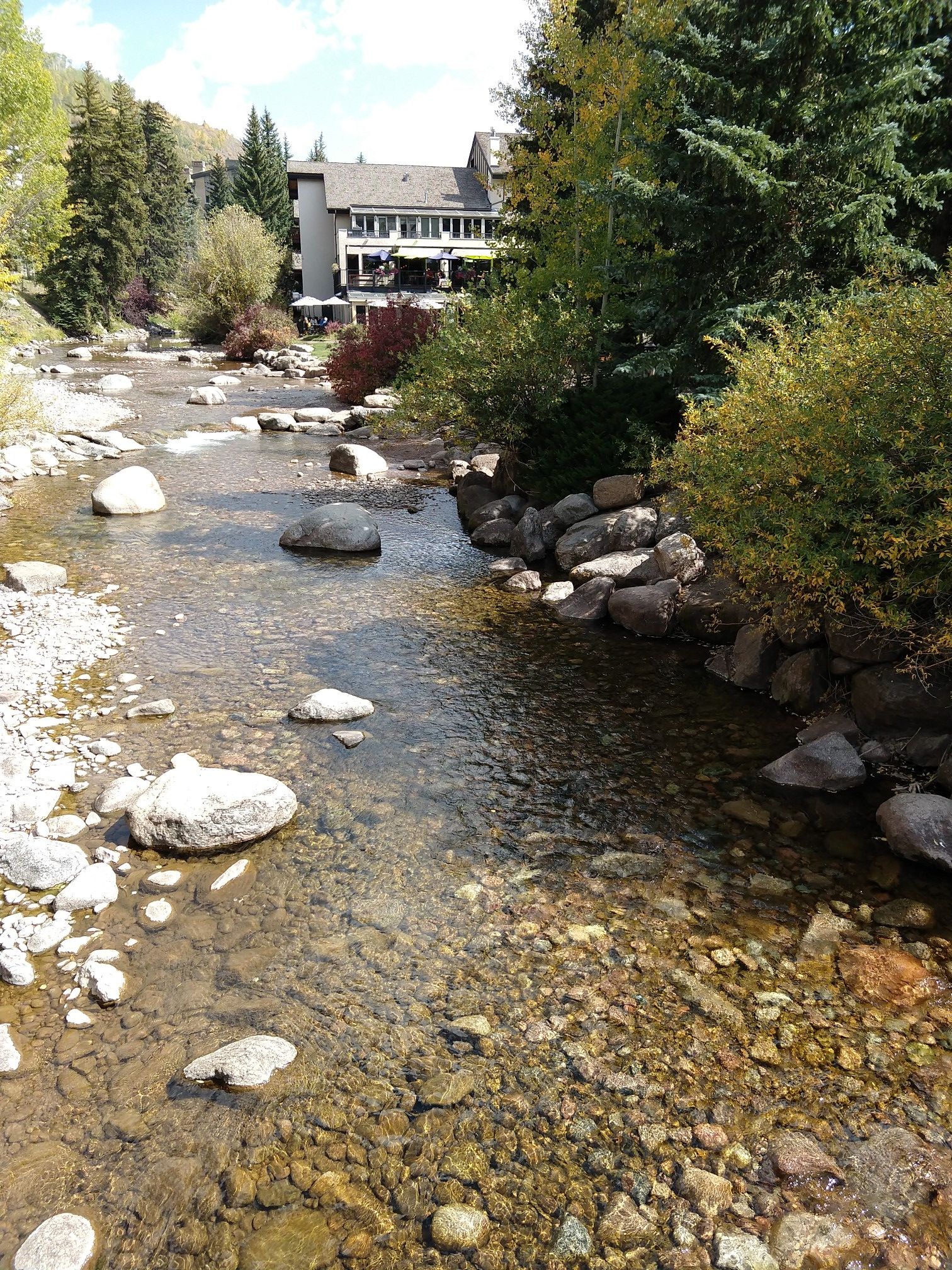 Clear stream flowing past a building and colorful autumn trees on a sunny day. - Gore Valley Trail