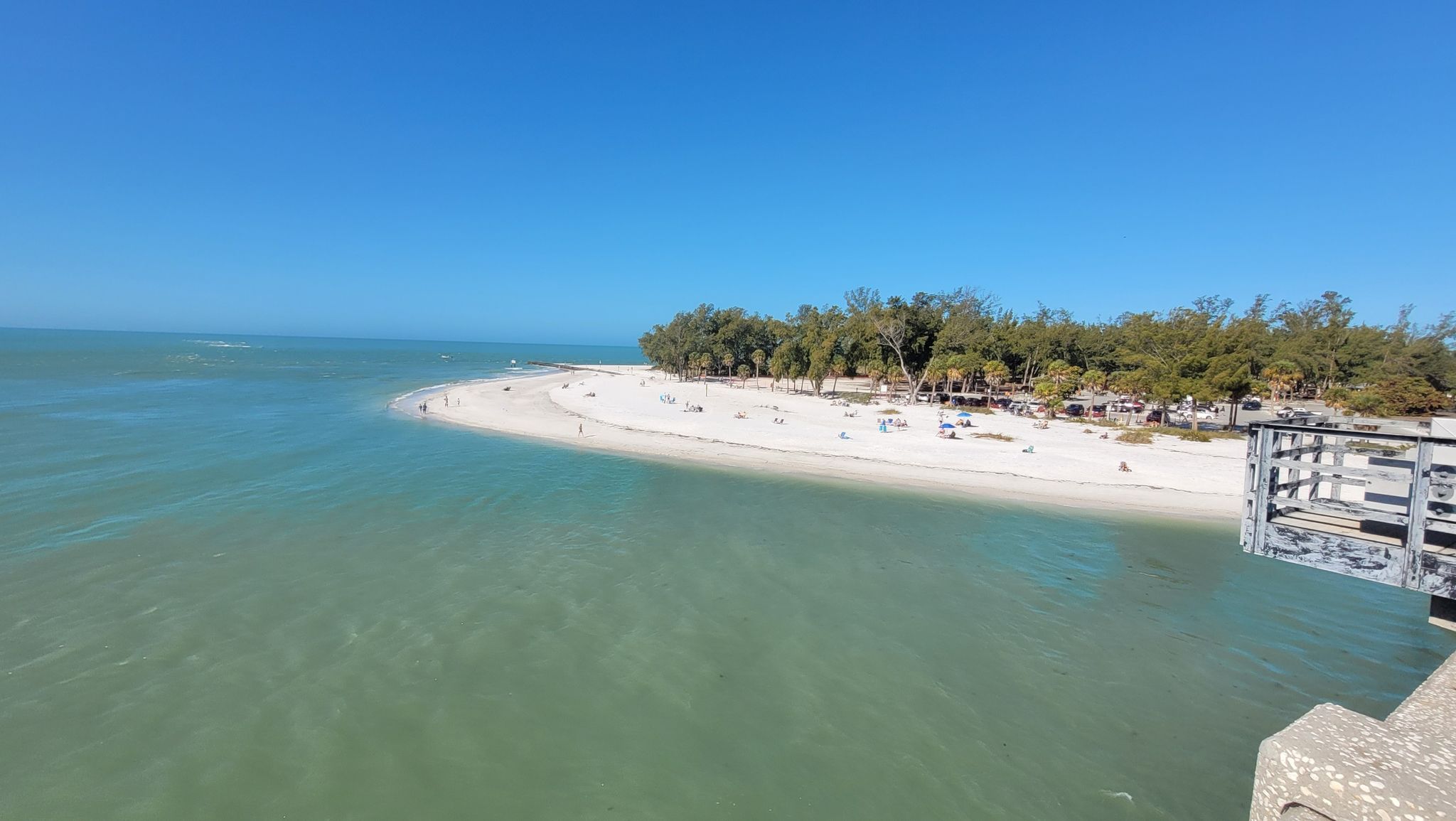 Aerial view of a white sand beach with people, clear water, and a pier. - Anna Maria Island loop