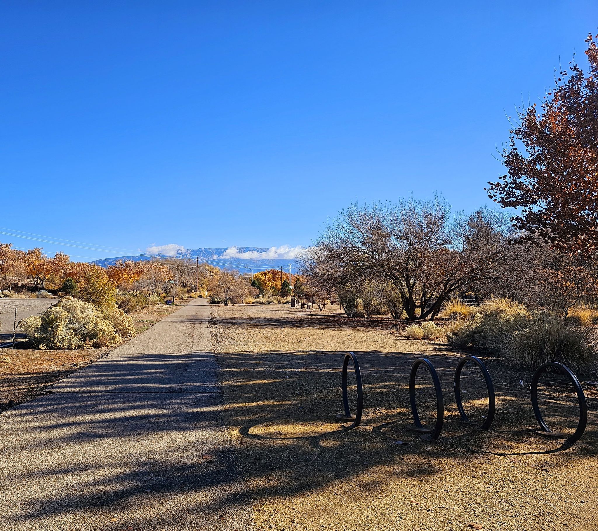 Paved path with bike racks, dry landscape, distant mountains under blue sky. - Rio Grande Sandy Beach Access – Alameda Trail loop from Alameda