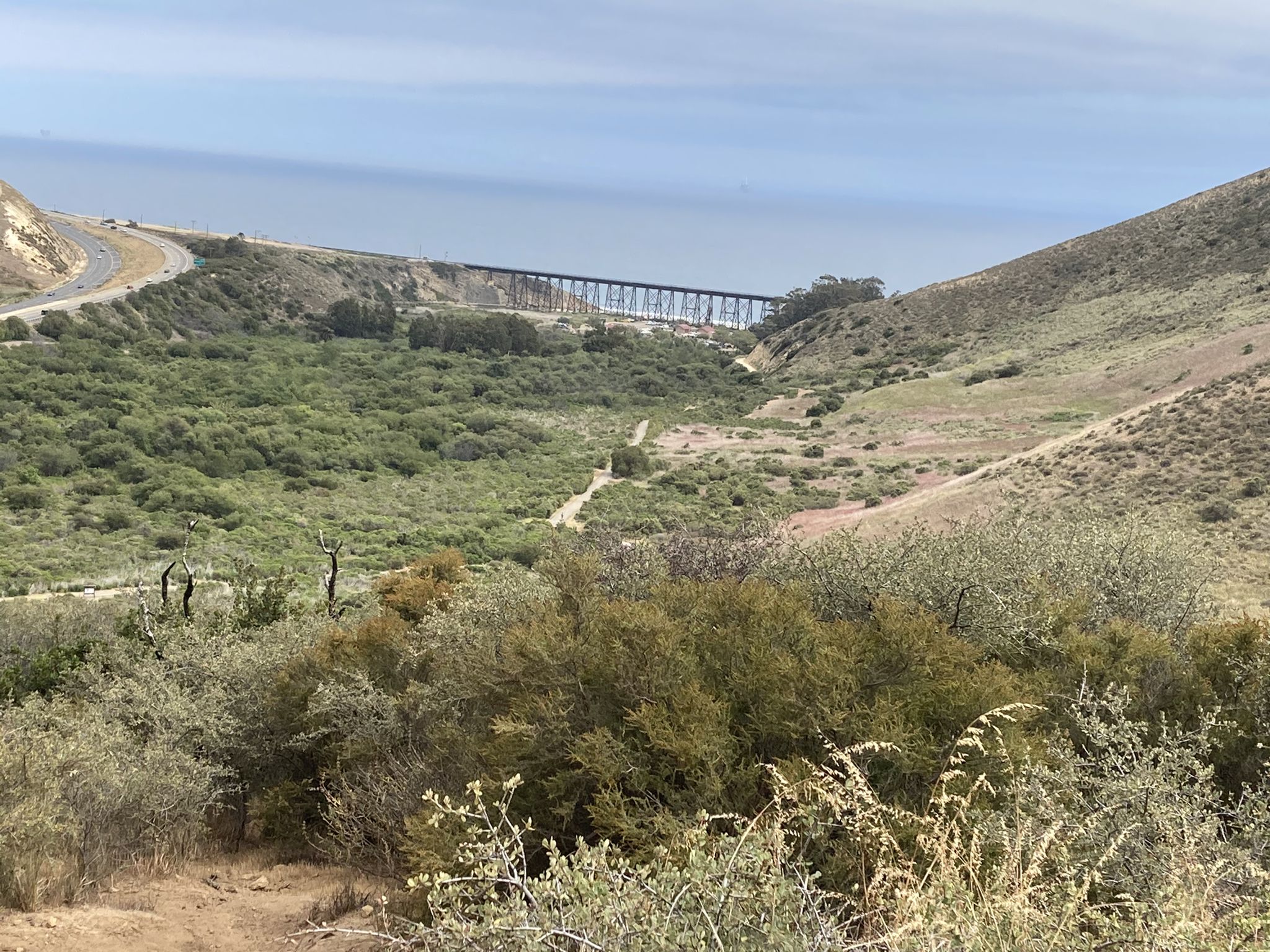 Expansive valley with a distant bridge, road, and ocean under bright daylight. - Gaviota Wind Caves Trail