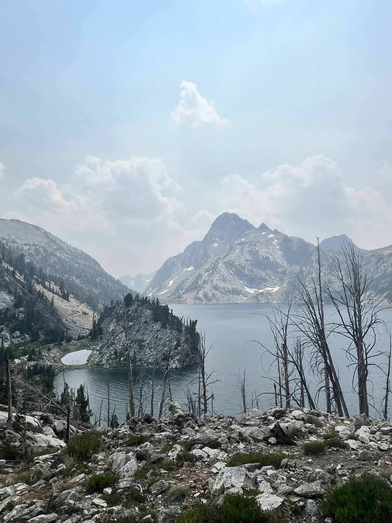 Hazy view of a mountain lake with rocky shores and distant peaks. - Grandjean Sawtooth Lake Loop