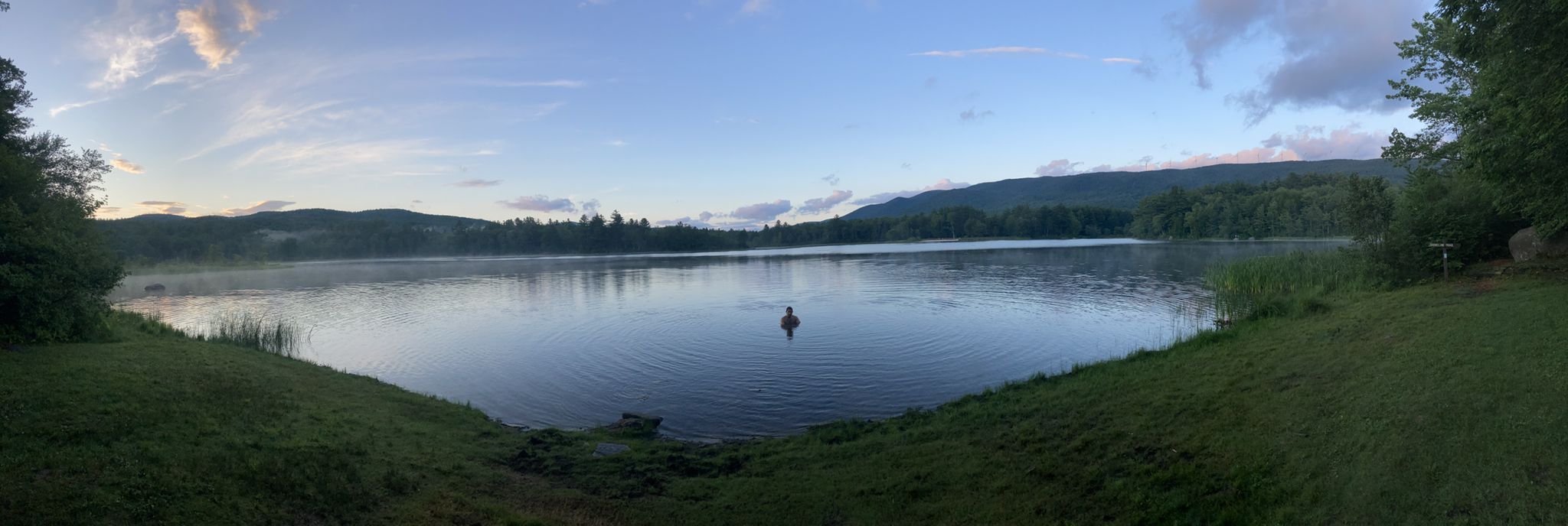 Person swimming in a calm lake surrounded by hills under a soft, cloudy sky. - Mauserts Pond Loop Trail