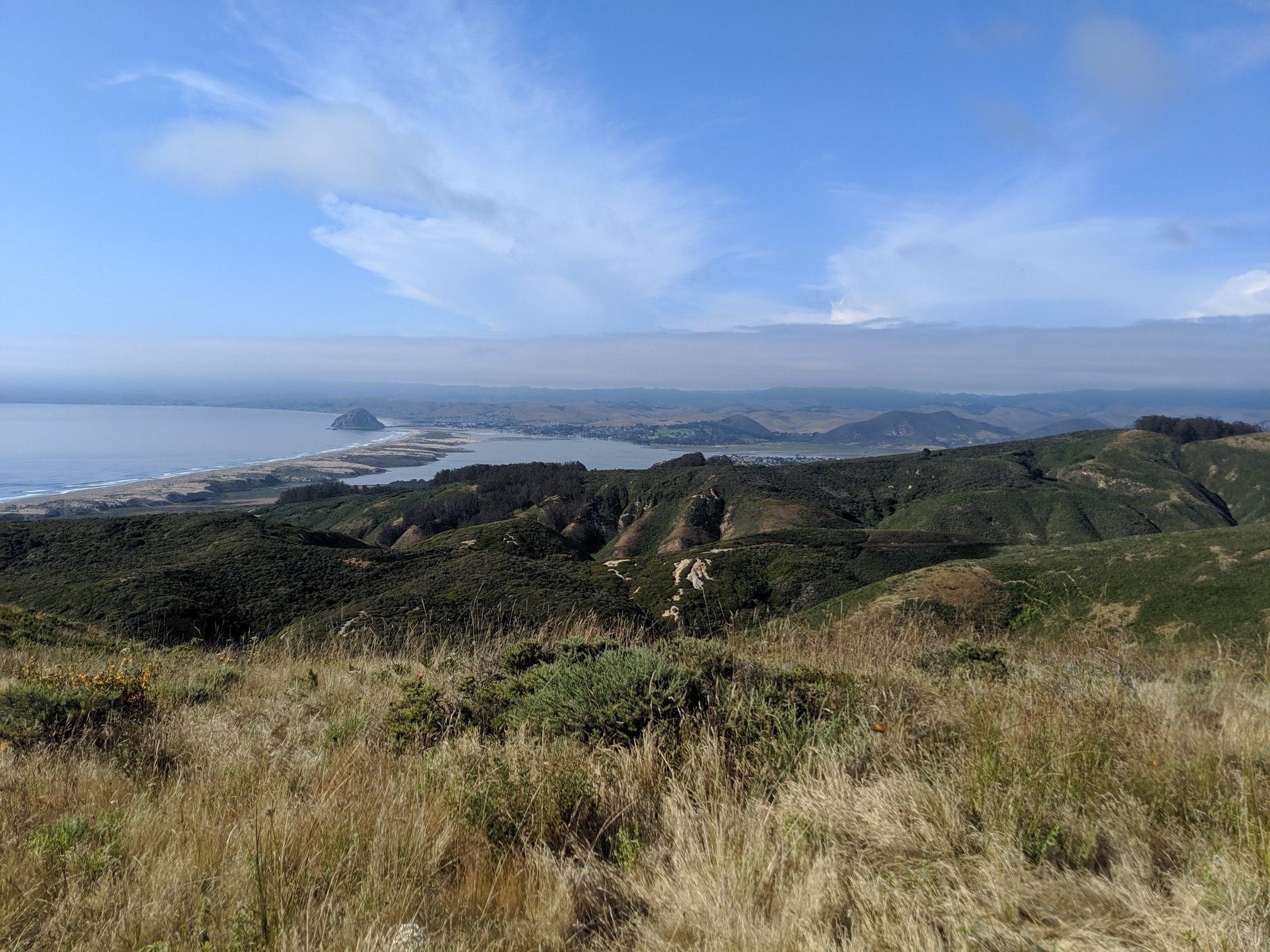 Vast coastal landscape with green hills, ocean, and a distant rock formation. - Oats Peak Trail – Spooner's Cove loop from Montaña de Oro State Park