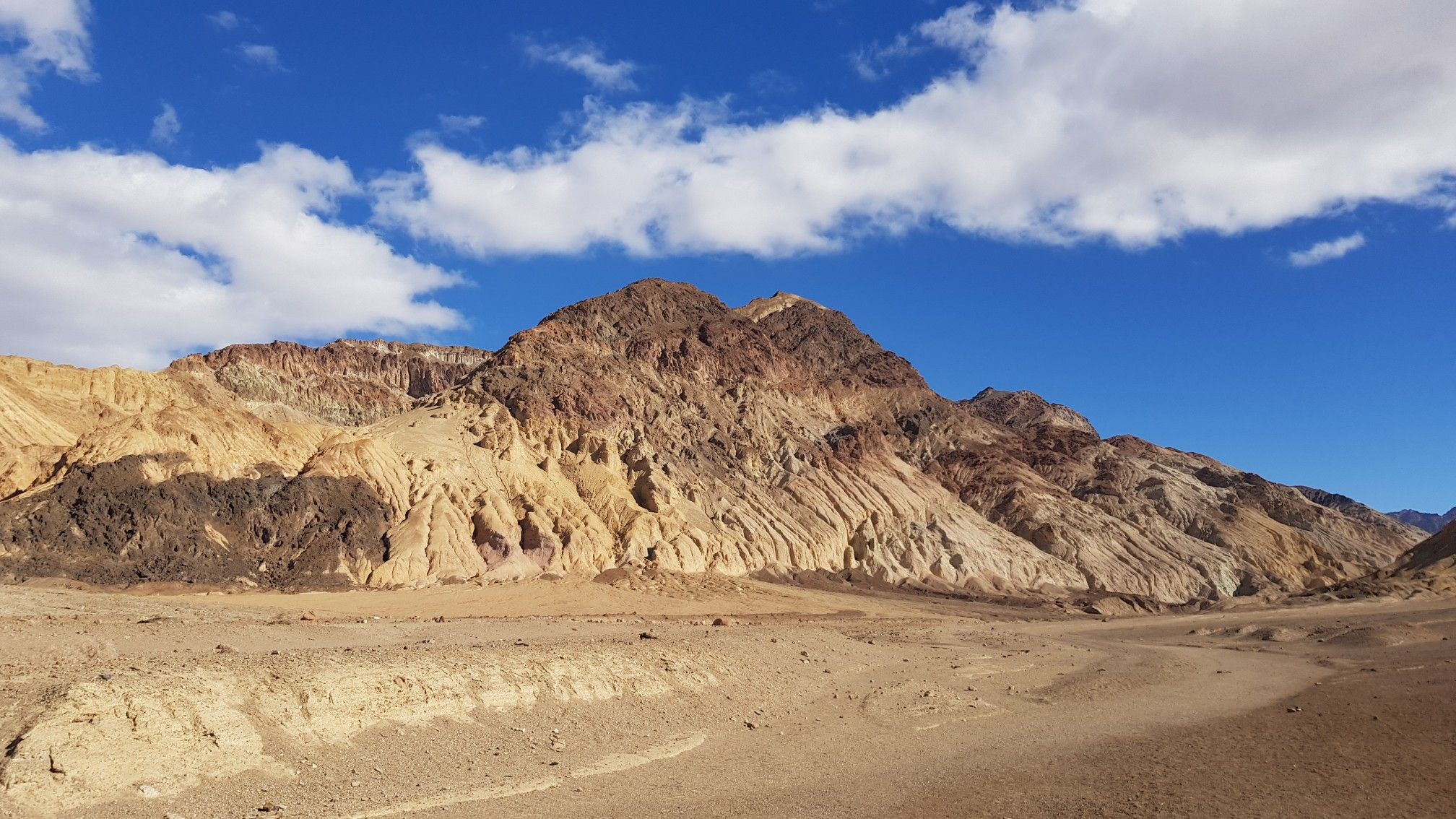 Colorful desert mountains rise under a bright blue sky with white clouds. - Desolation Canyon Trail