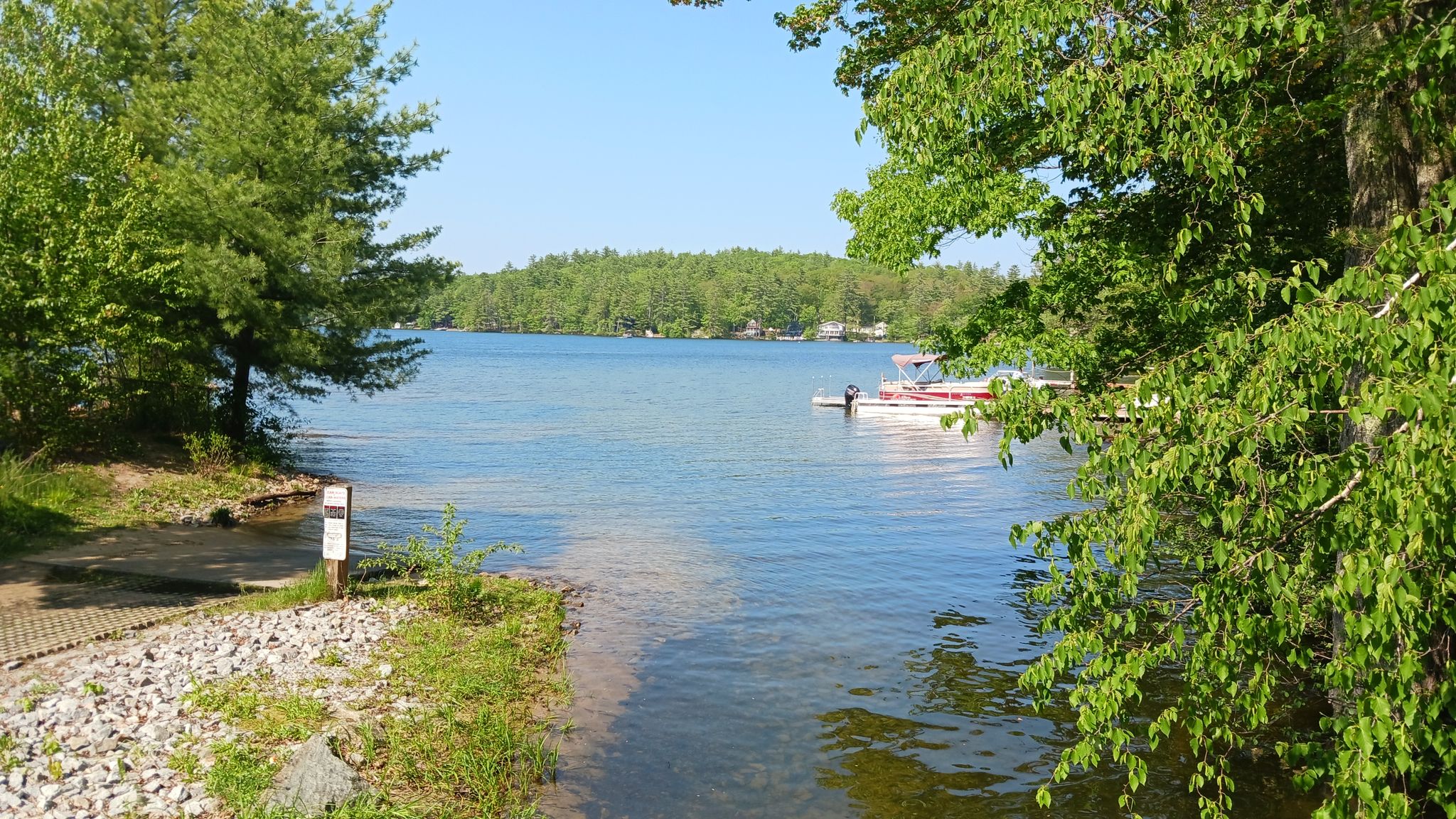 A boat launch leading into a wide lake with a distant boat. - Webster Lake loop road run