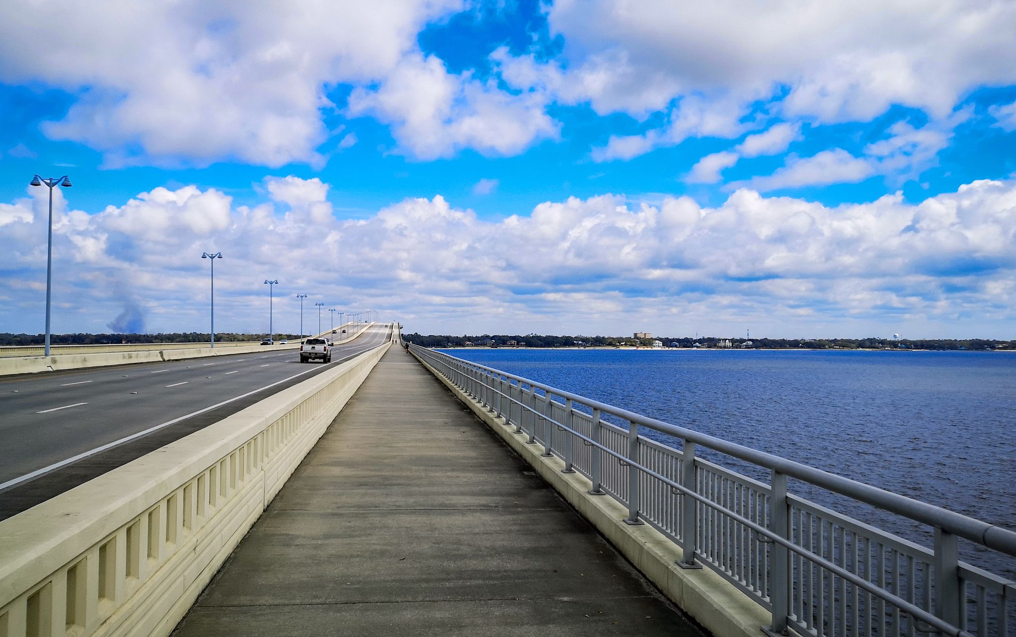 Long bridge over blue water with cars, under a bright blue sky with clouds. - Biloxi Bay Bridge loop from Maritime and Seafood Industry Museuem